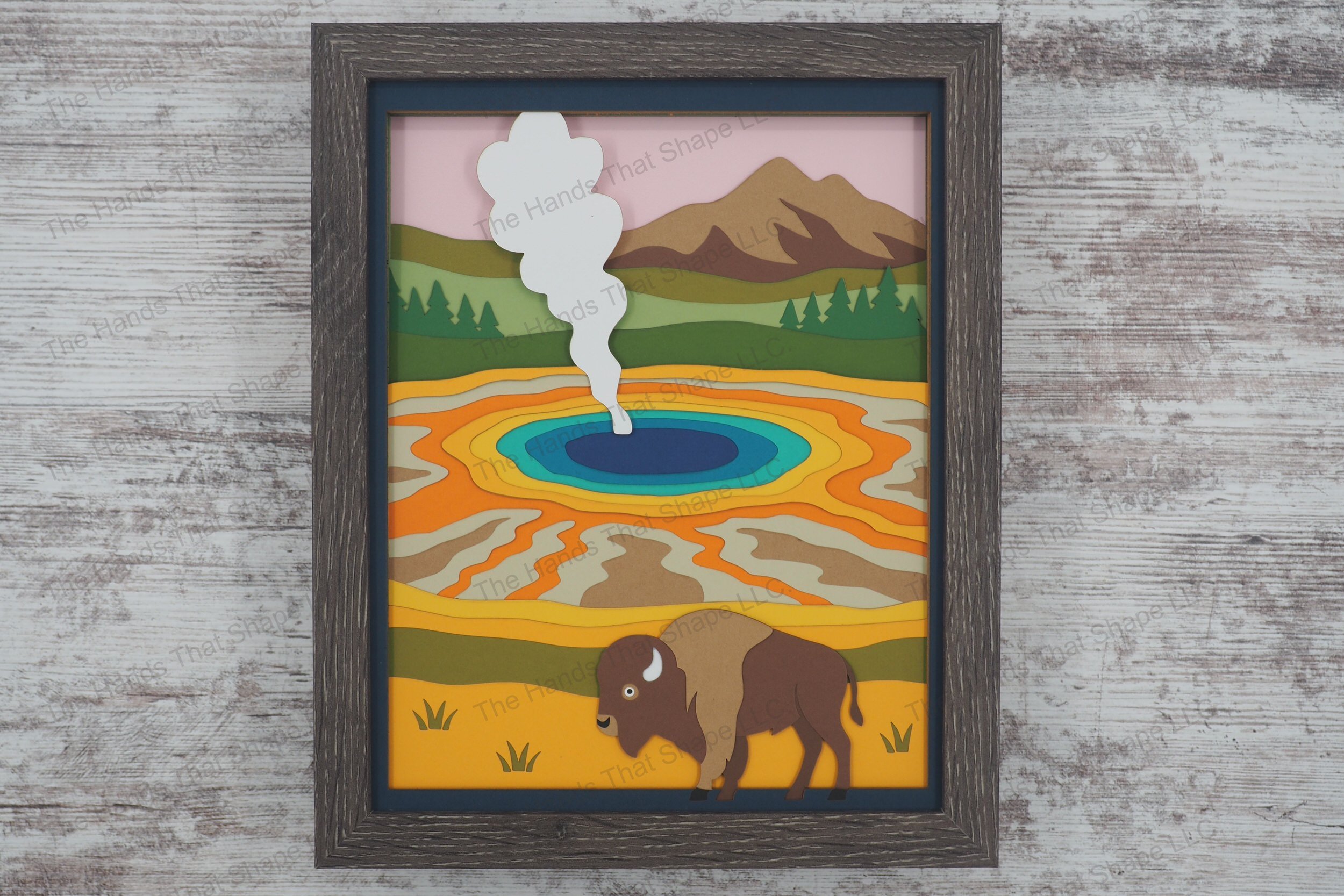 A richly layered 3D layered paper shadowbox featuring a classic Yellowstone scene with a lone bison standing before a vibrant prismatic hot spring.