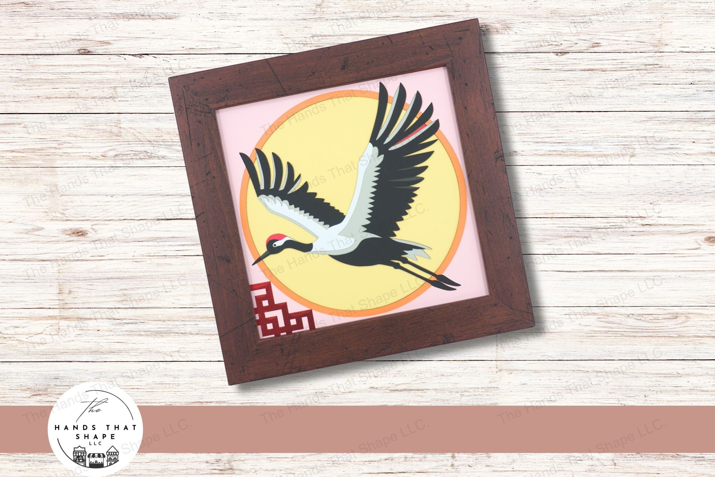 This layered cardstock art piece features a majestic Japanese red-crowned crane soaring through the air with wings fully outstretched.