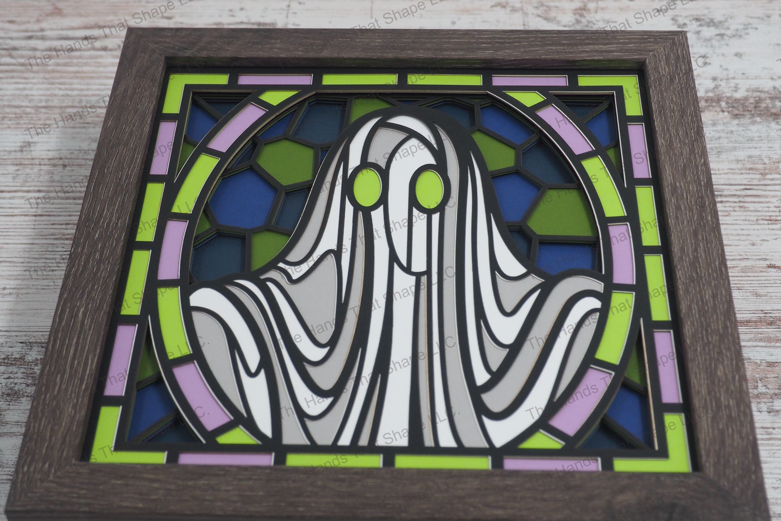 A visually striking layered paper shadowbox depicting a ghost crafted in a stained glass style with curves featuring piercing bright green eyes.