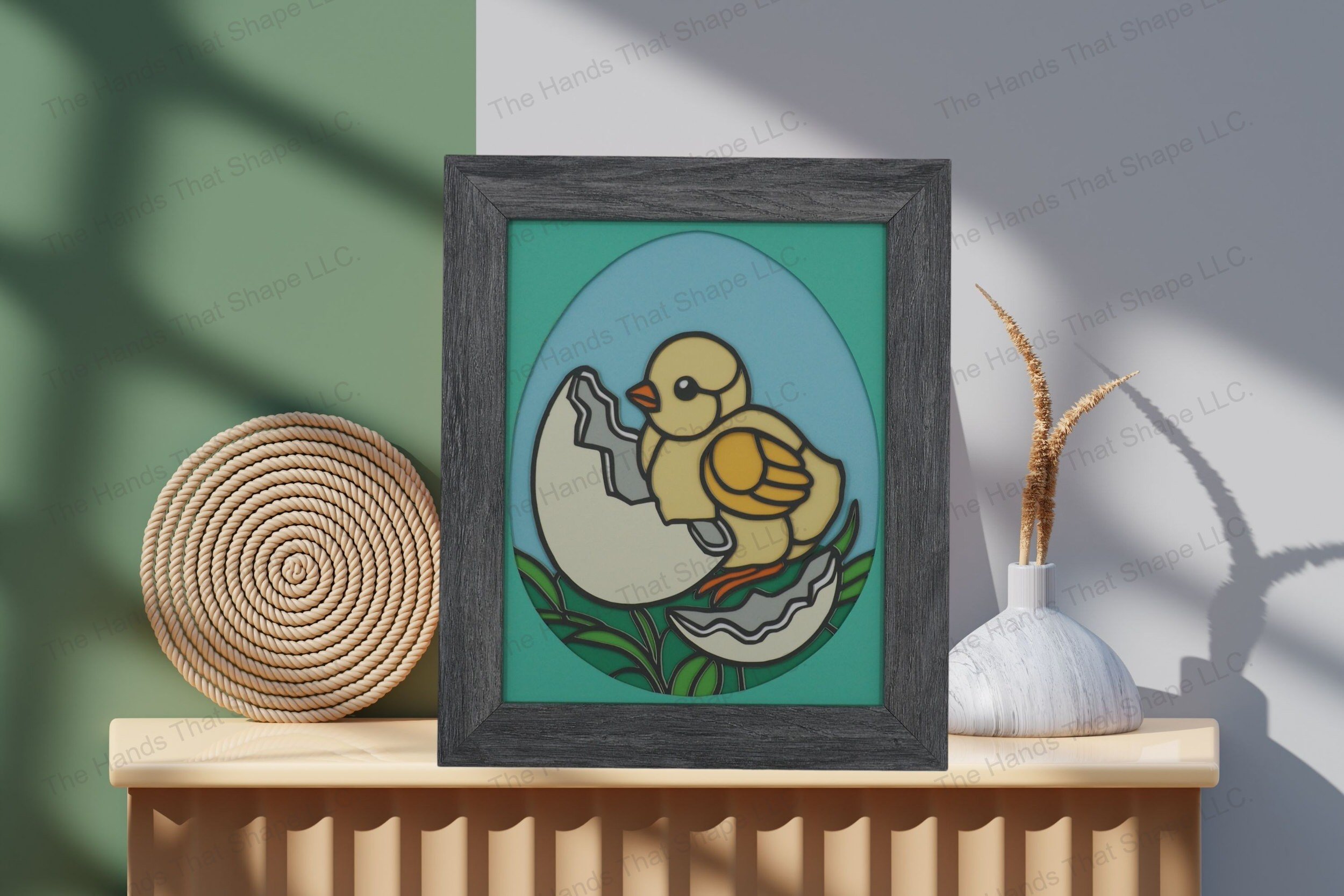 Admire this charming baby chick-themed cardstock artwork, thoughtfully displayed on a table, showcasing its colorful layers and whimsical egg-shaped design.