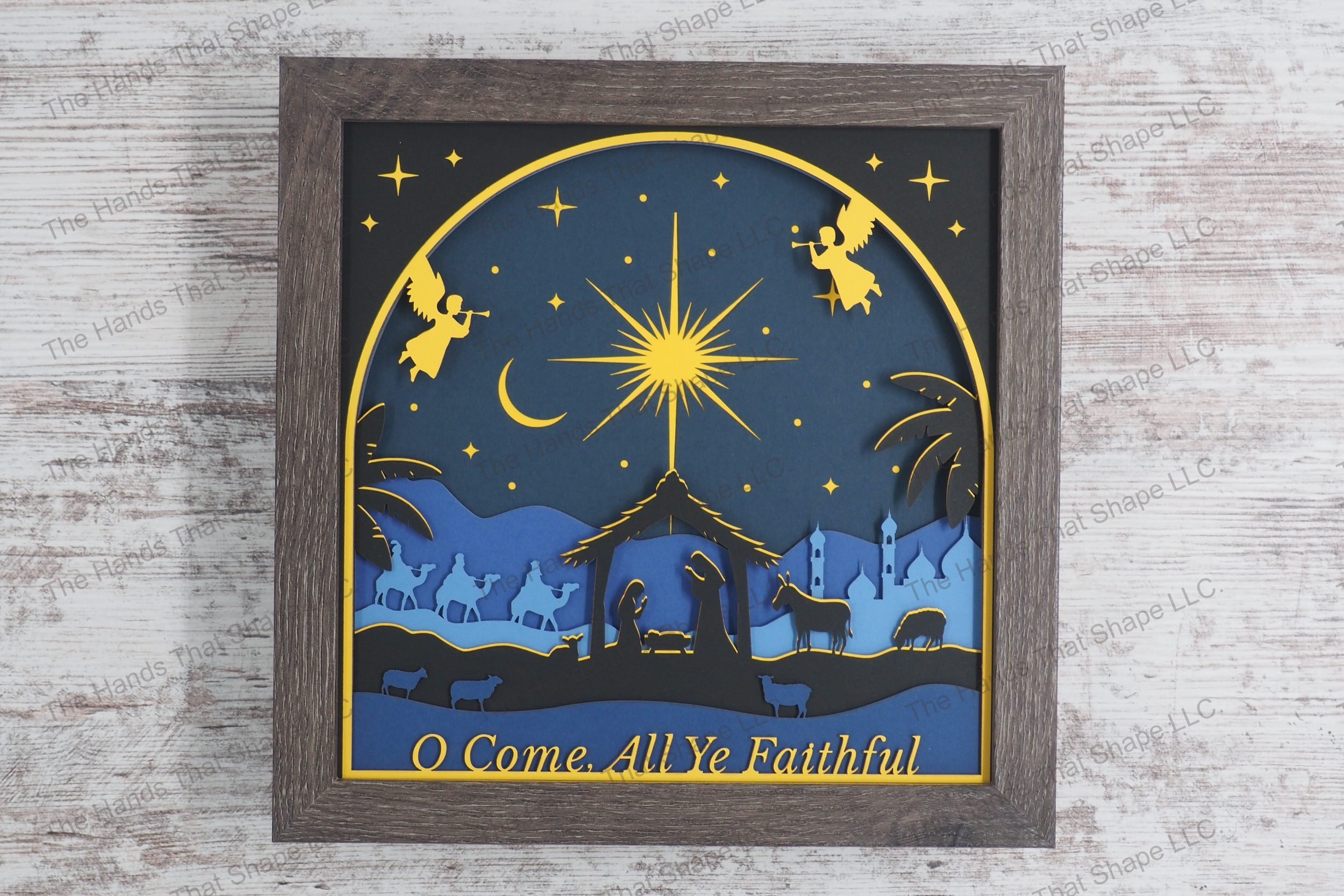 A detailed framed layered paper shadowbox depicting the nativity scene with silhouettes of the Holy Family, animals, wise men, and celestial angels.