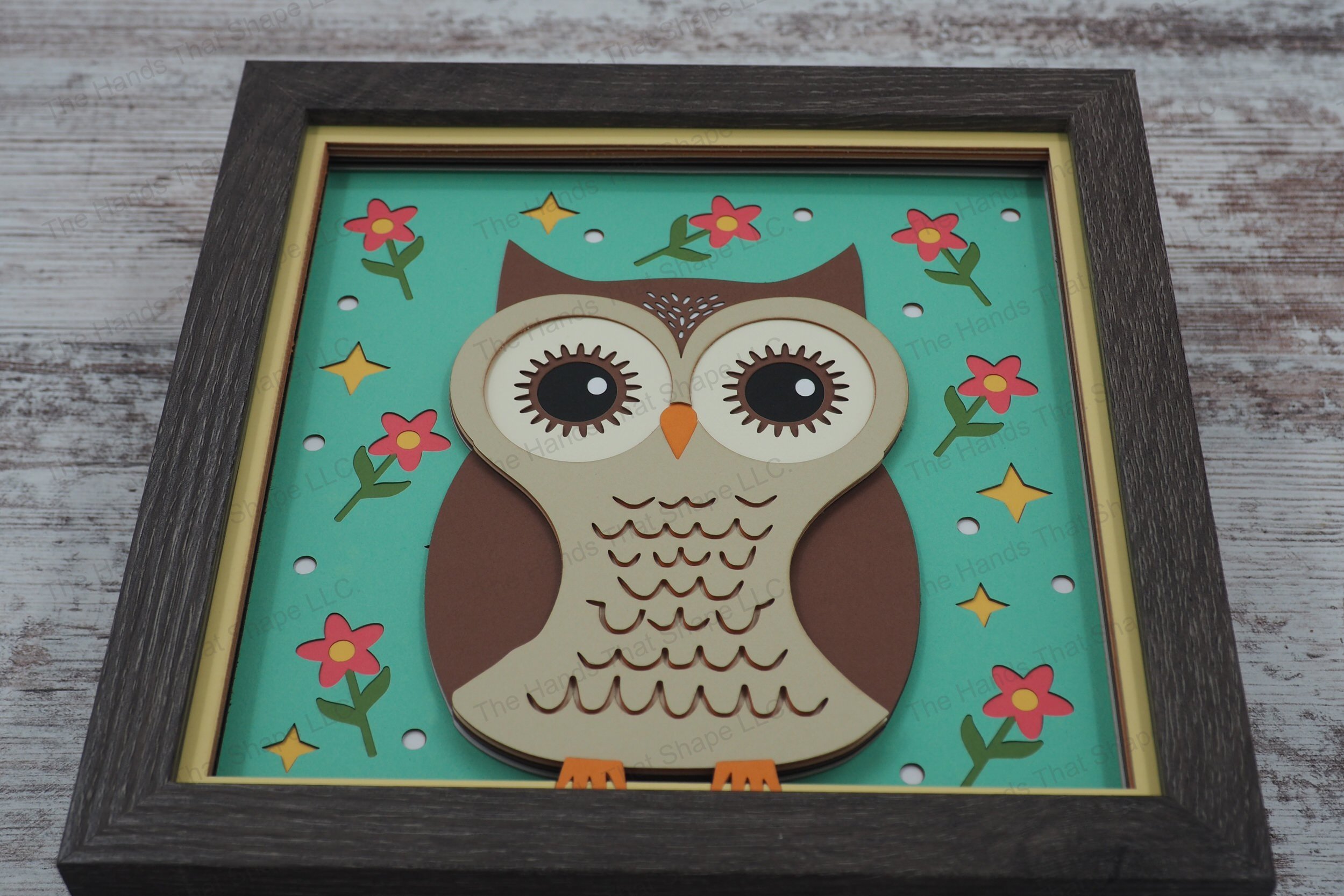 This layered paper shadowbox features a folksy owl with expressive eyes surrounded by flowers, dots, and stars, adding enchantment and warmth to any room.