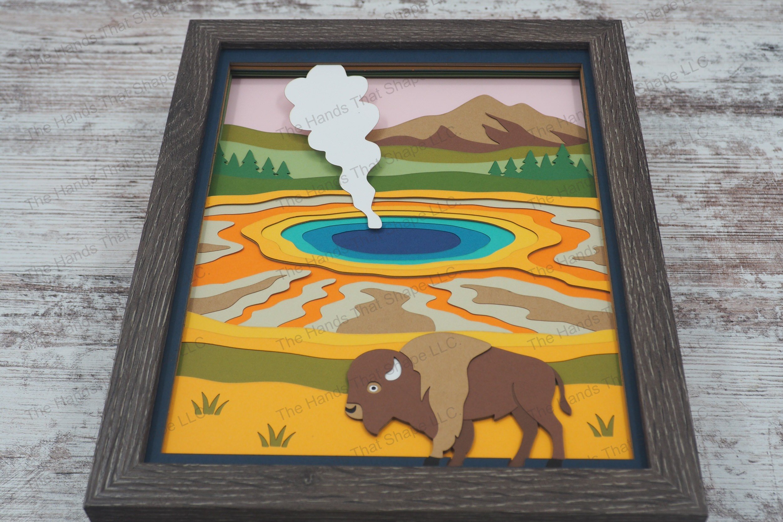 A richly layered 3D layered paper shadowbox featuring a classic Yellowstone scene with a lone bison standing before a vibrant prismatic hot spring.
