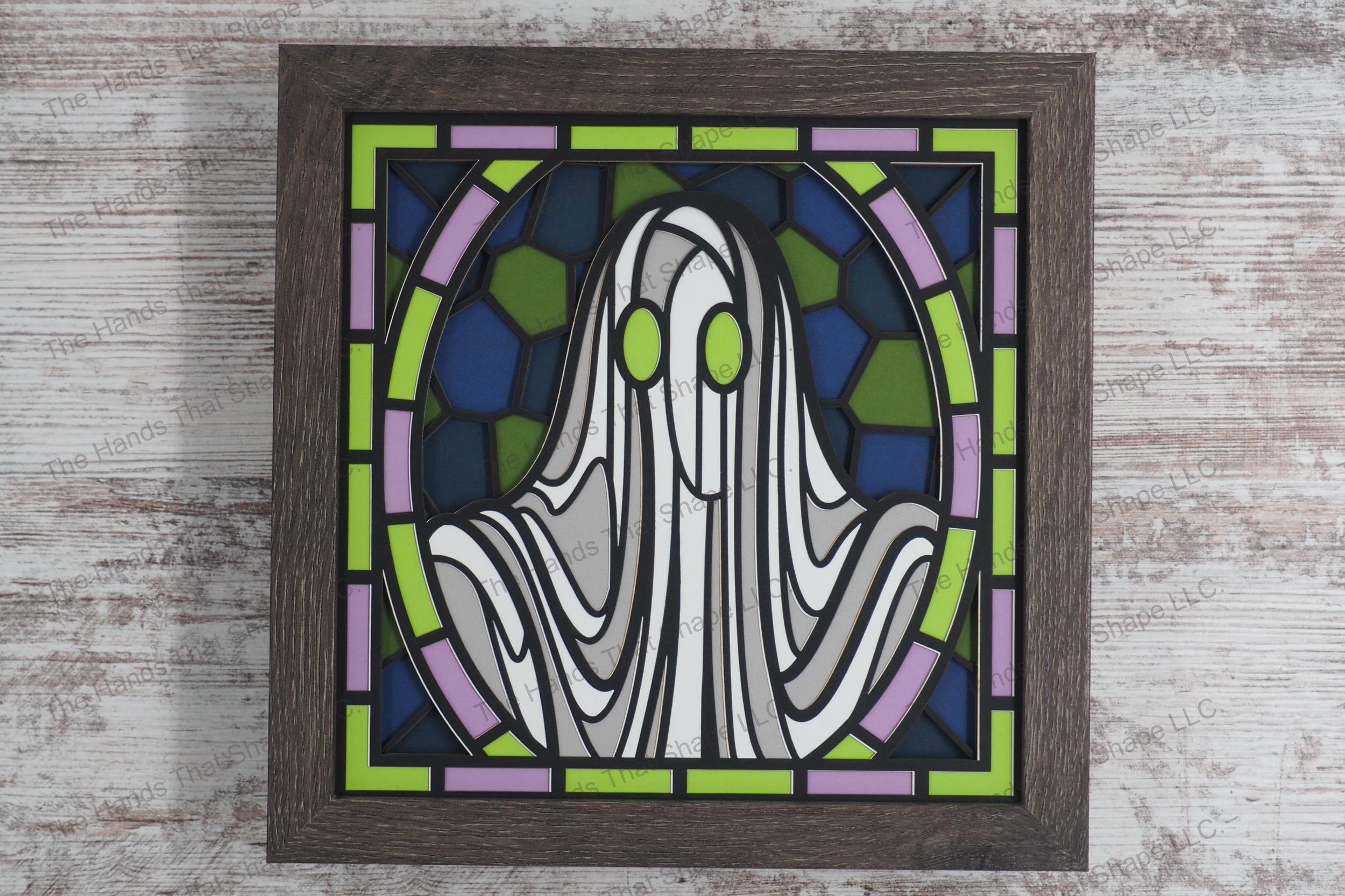 A visually striking layered paper shadowbox depicting a ghost crafted in a stained glass style with curves featuring piercing bright green eyes.