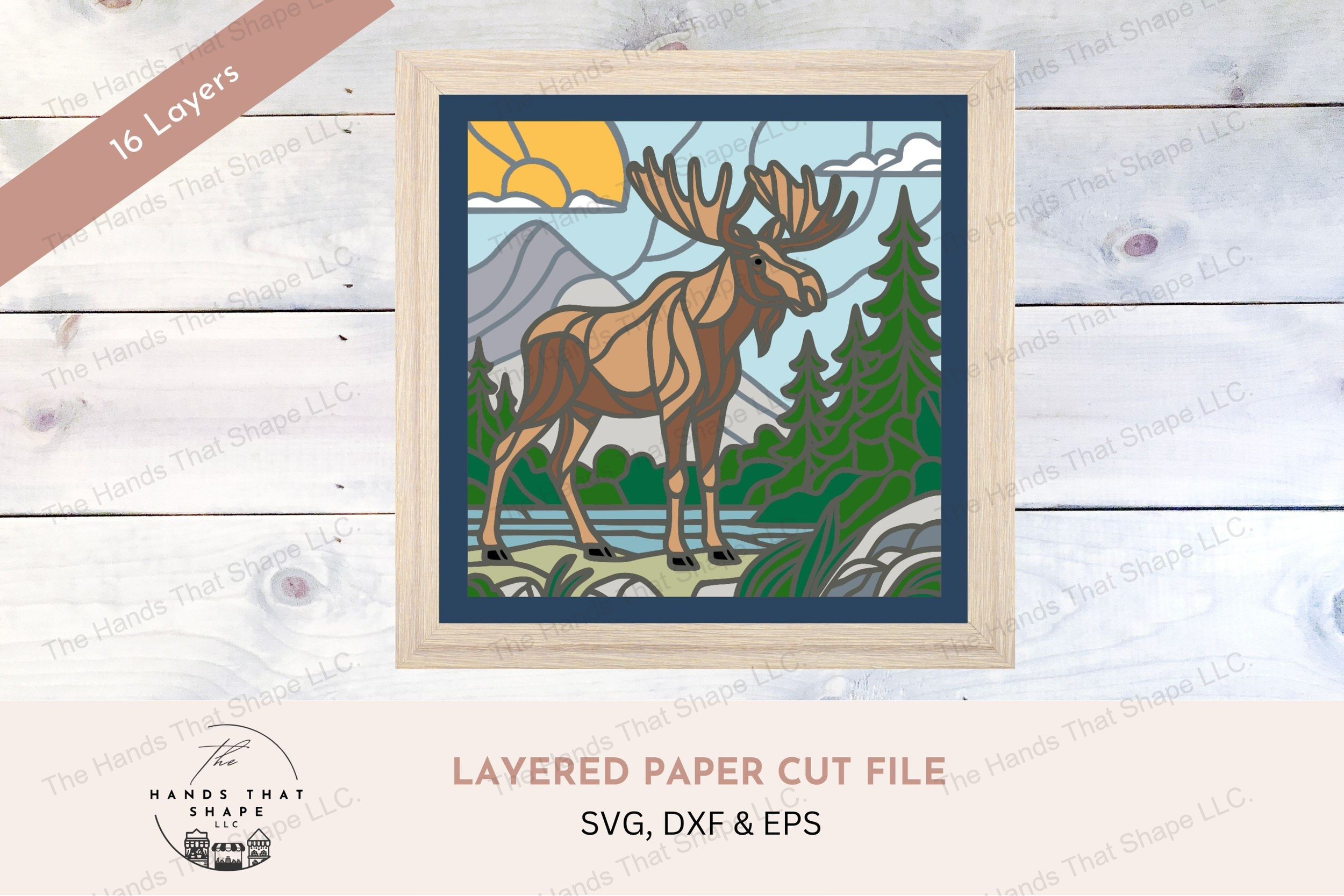 This layered cardstock art piece vividly captures a moose by the water’s edge, surrounded by mountains and trees, creating a striking stained glass effect.