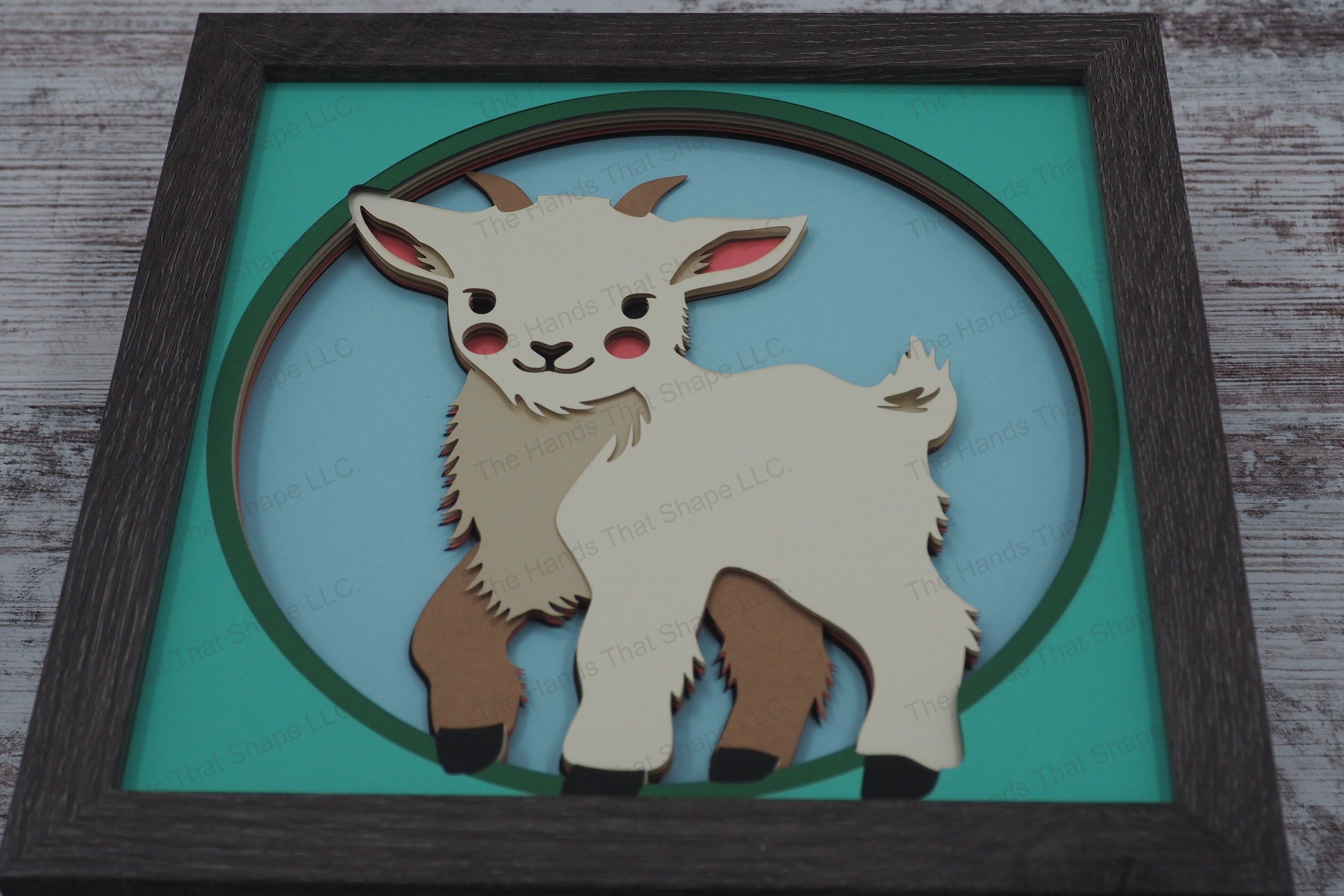 This layered paper art shadowbox captures the charm of a sweet baby goat, standing curiously and looking directly at the viewer in a whimsical 3D display
