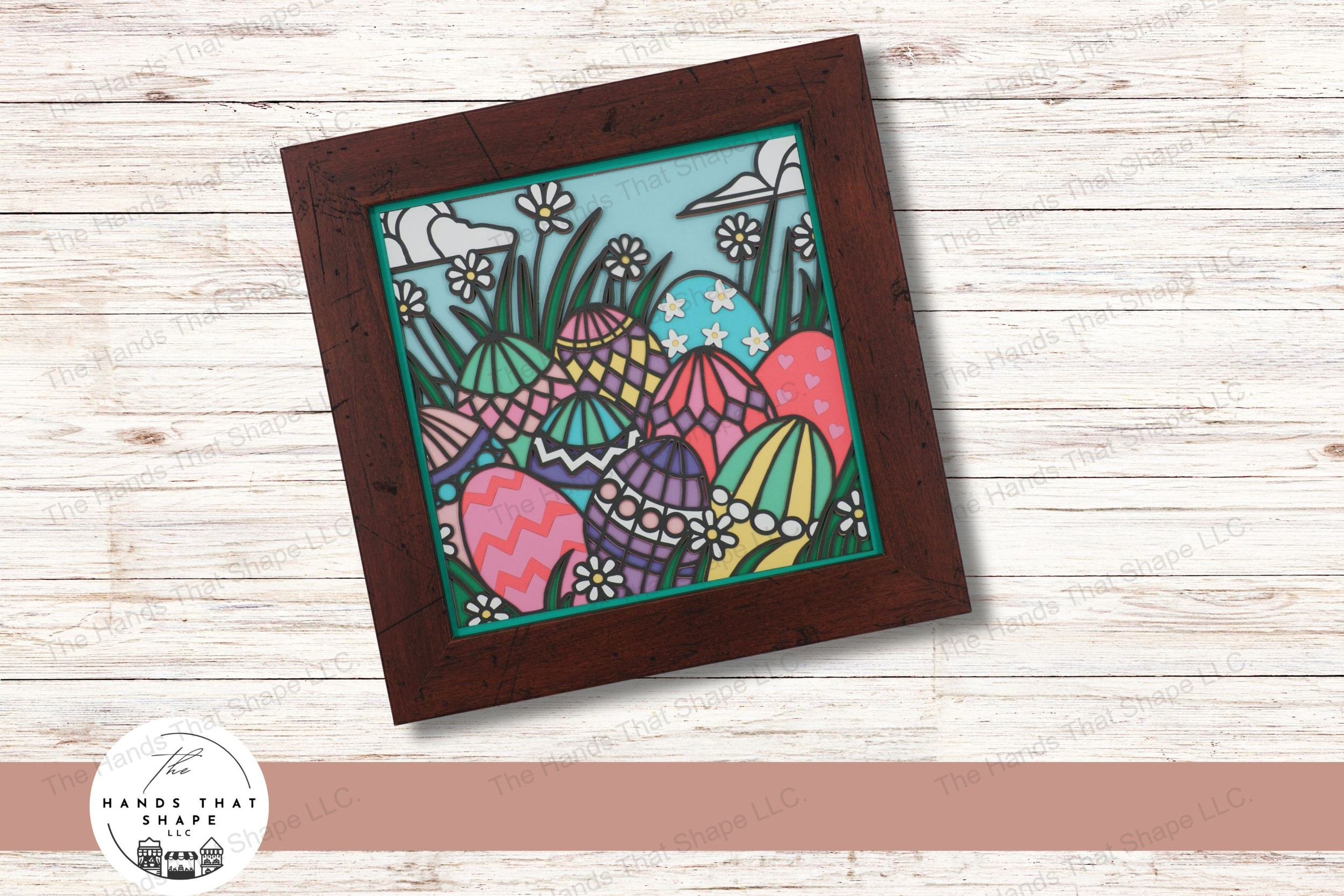 This layered cardstock art piece captures a delightful Easter scene, featuring decorated eggs nestled among daisies in the grass and set under a sky of clouds.