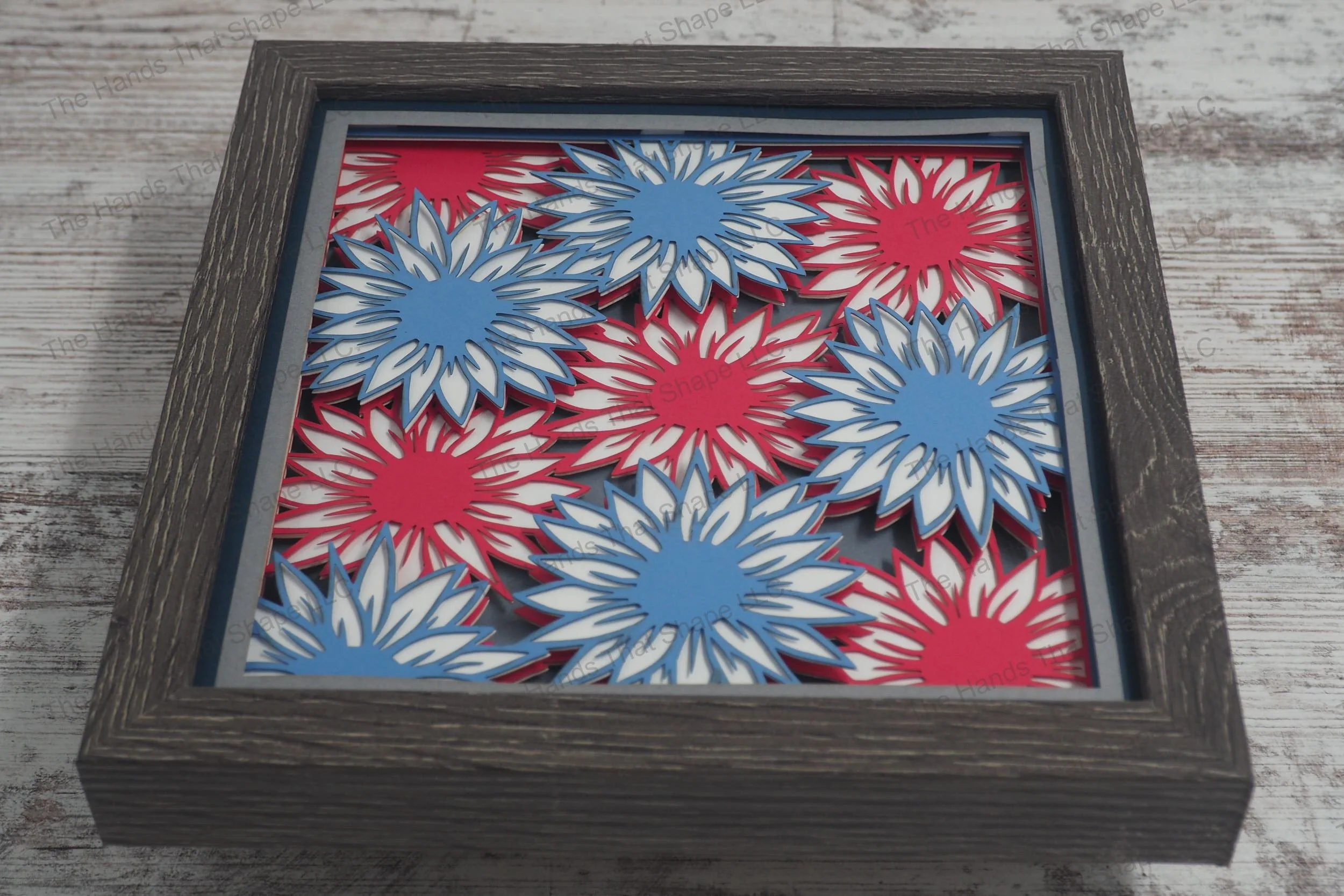 A layered paper shadowbox featuring a patriotic display of blue, white, and red flowers resembling fireworks, available without text