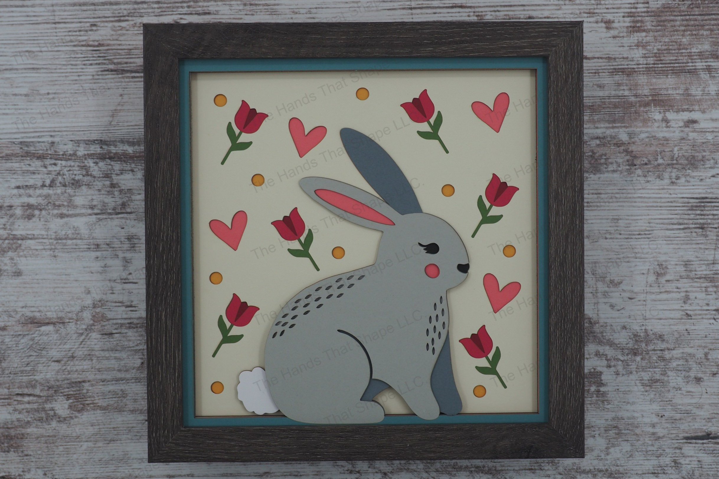 Charming layered paper shadowbox features a folksy bunny surrounded by tulips, hearts, and dots, perfect for bringing springtime warmth and joy to any space.