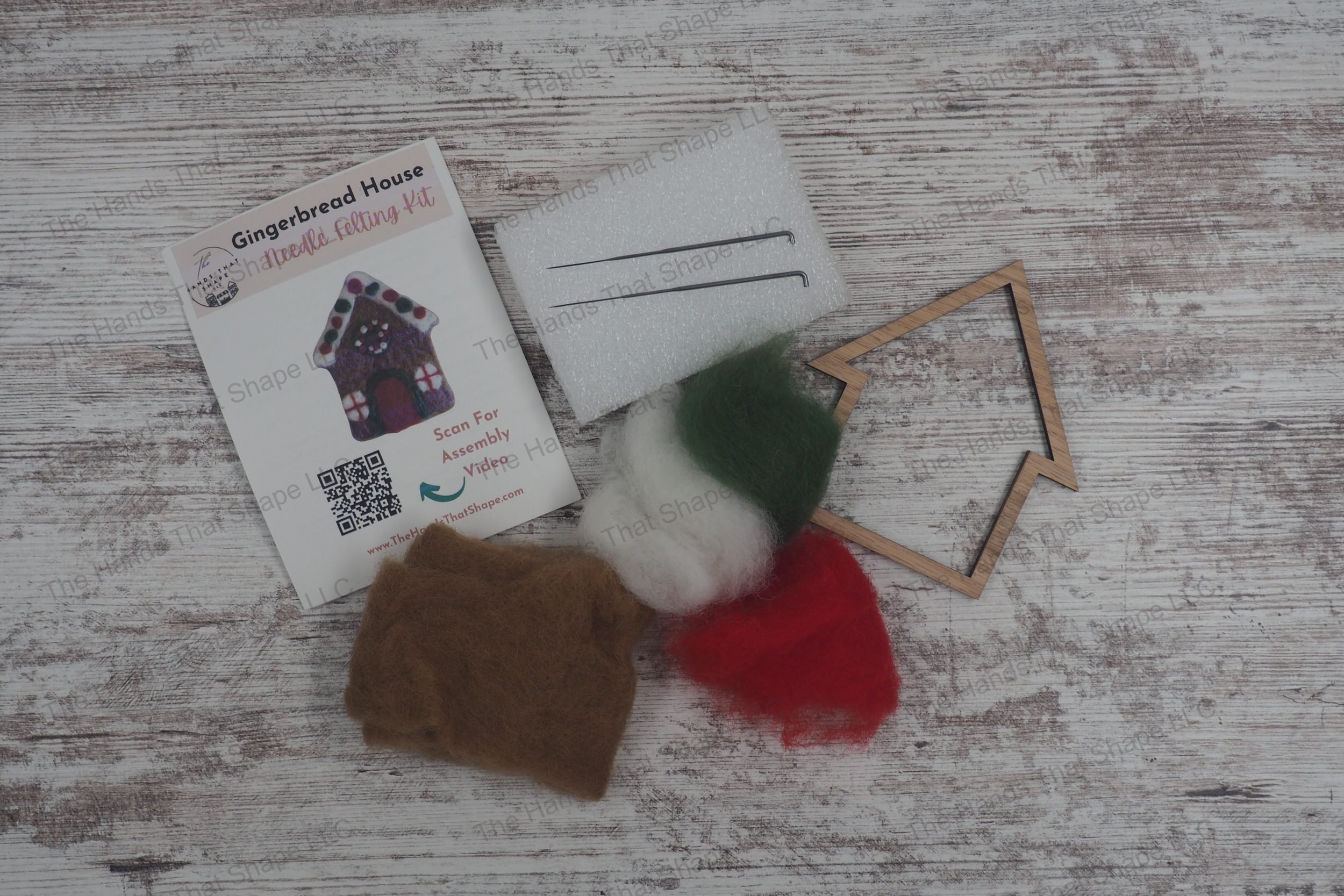 Craft a festive gingerbread house with this needle felting kit featuring colored wools, felting needles, a foam pad, and a wooden frame template.