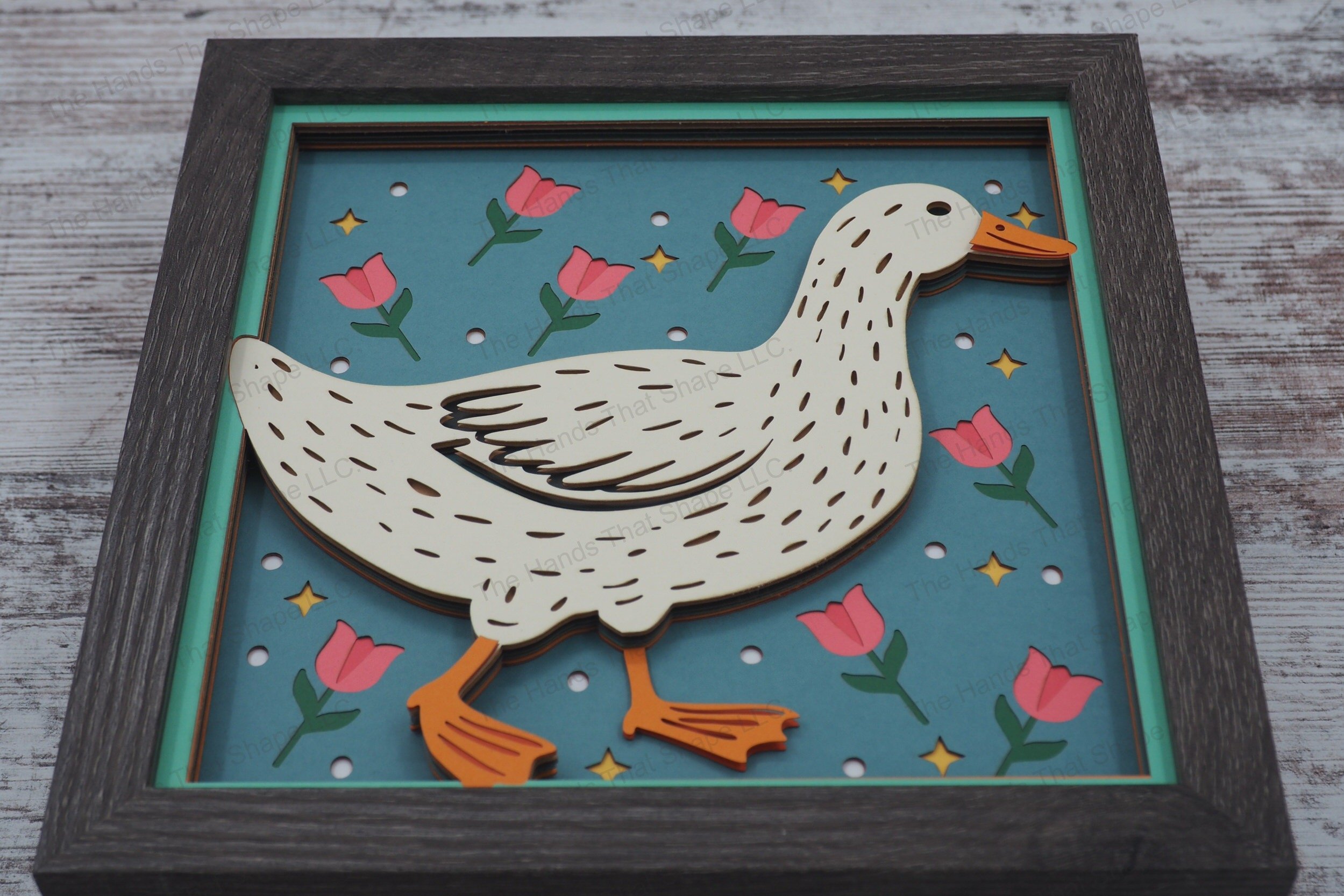 This delightful 3D layered paper shadowbox features a charming folksy duck strolling amidst vibrant tulips, whimsical dots, and sparkling stars.