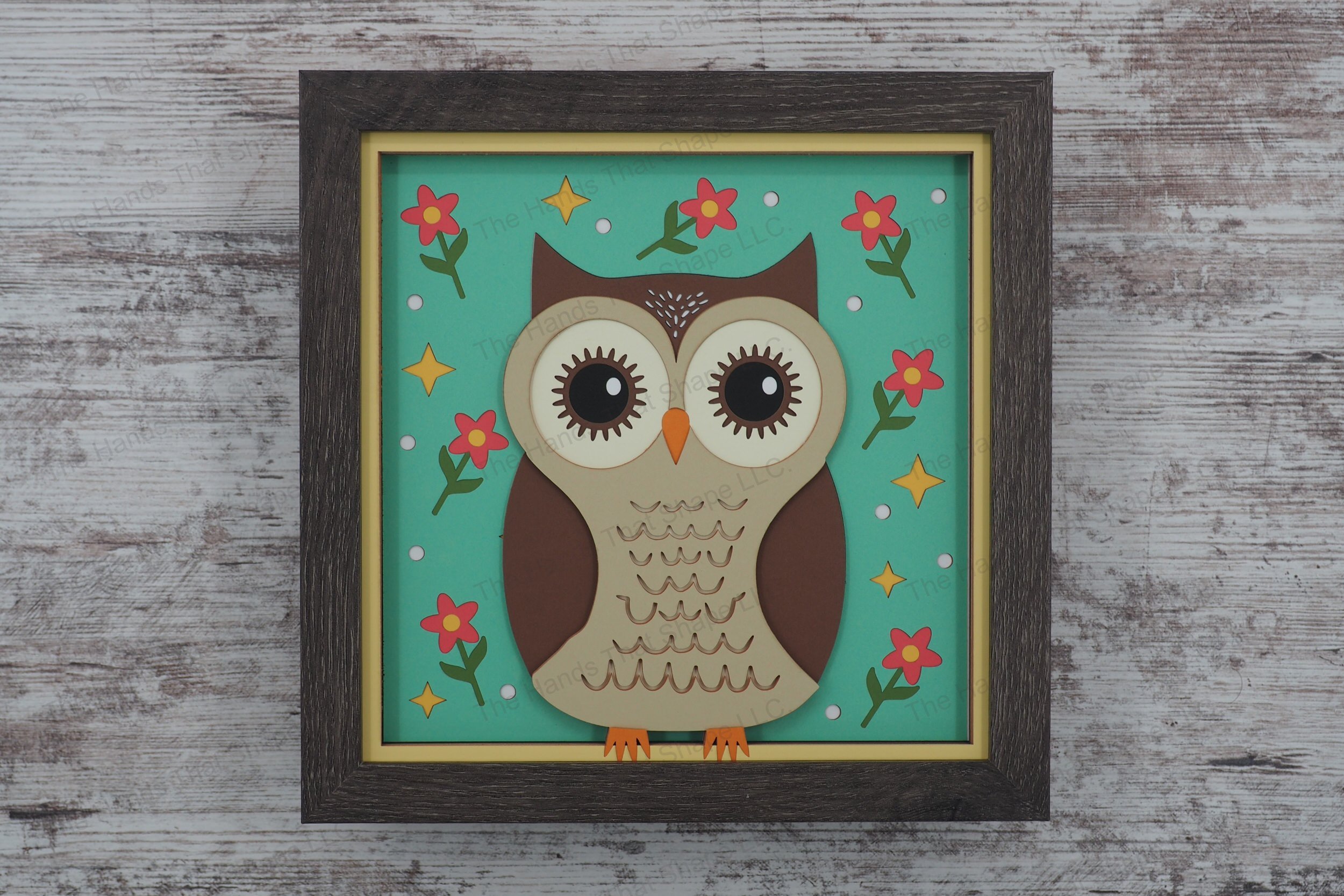 This layered paper shadowbox features a folksy owl with expressive eyes surrounded by flowers, dots, and stars, adding enchantment and warmth to any room.