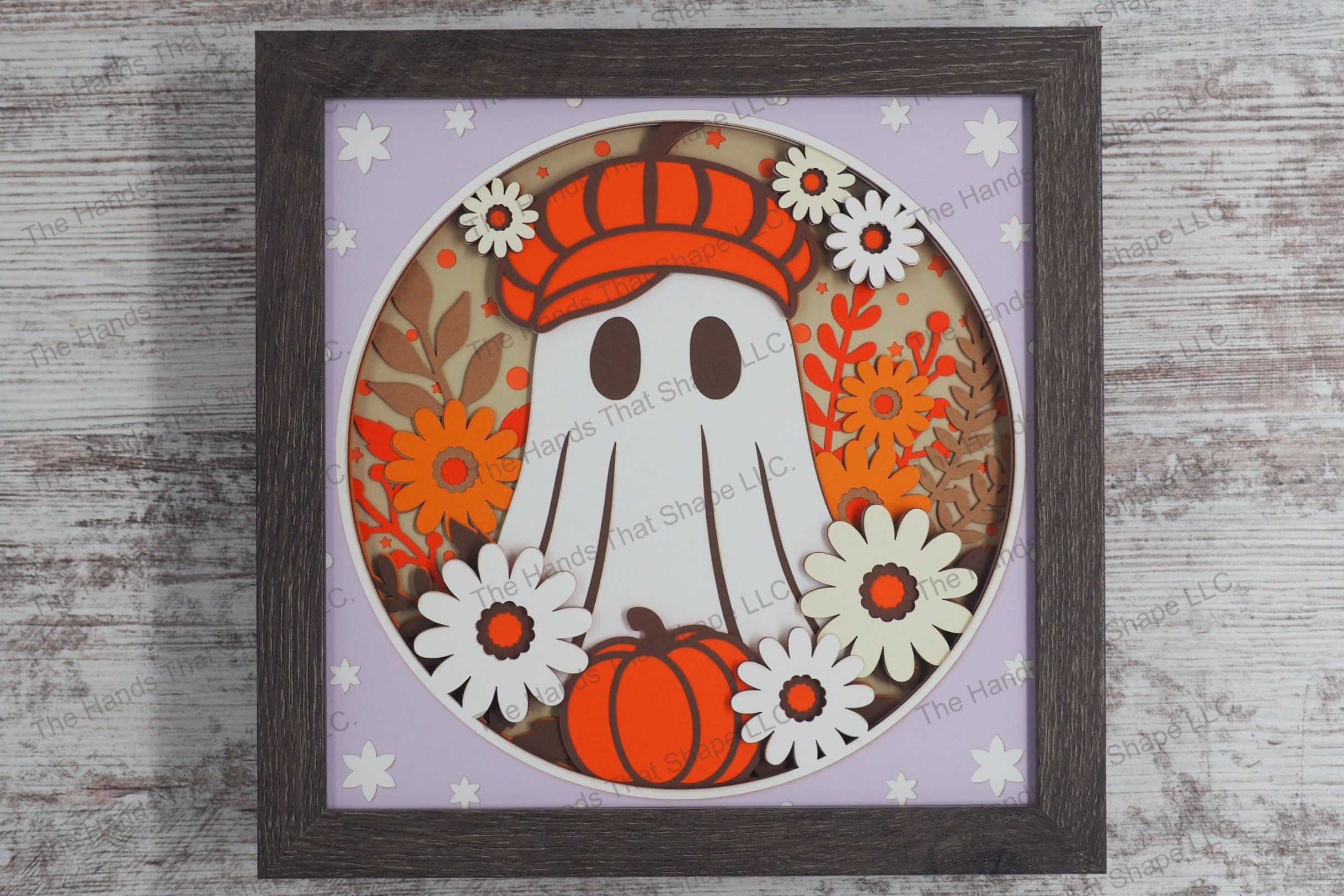 A framed playful layered paper shadowbox depicting a friendly ghost adorned with a hat, surrounded by vibrant fall flowers and a pumpkin.