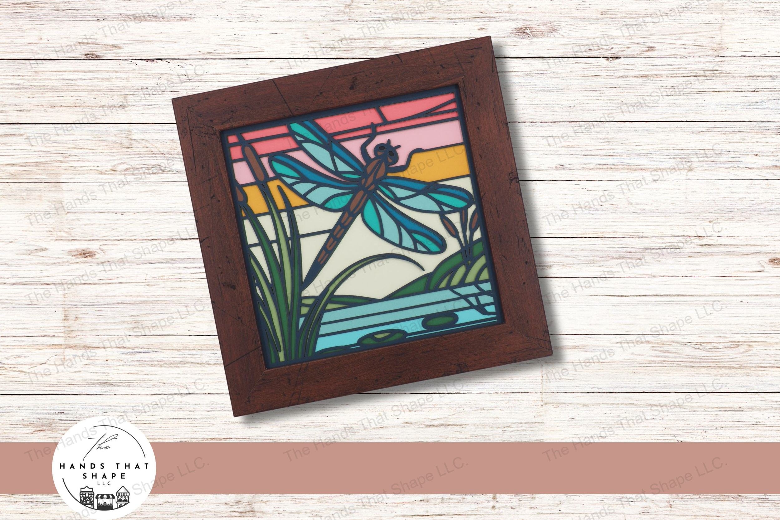This captivating layered cardstock art piece features a dragonfly by the water's edge, surrounded by cattails and lily pads illuminated by a fresh sunrise.
