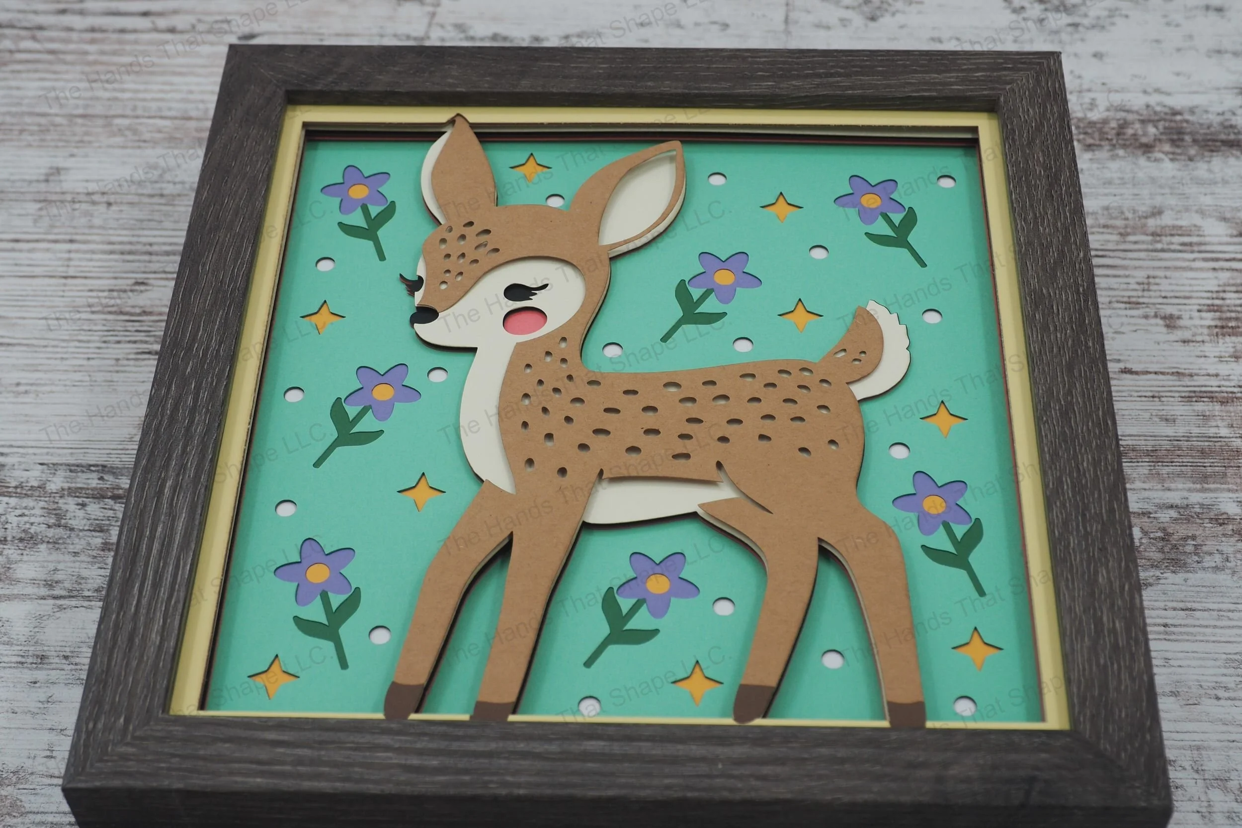 This enchanting 3D layered paper shadowbox depicts a folksy fawn, surrounded by flowers, dots, and stars, perfect for adding whimsy to your home décor.
