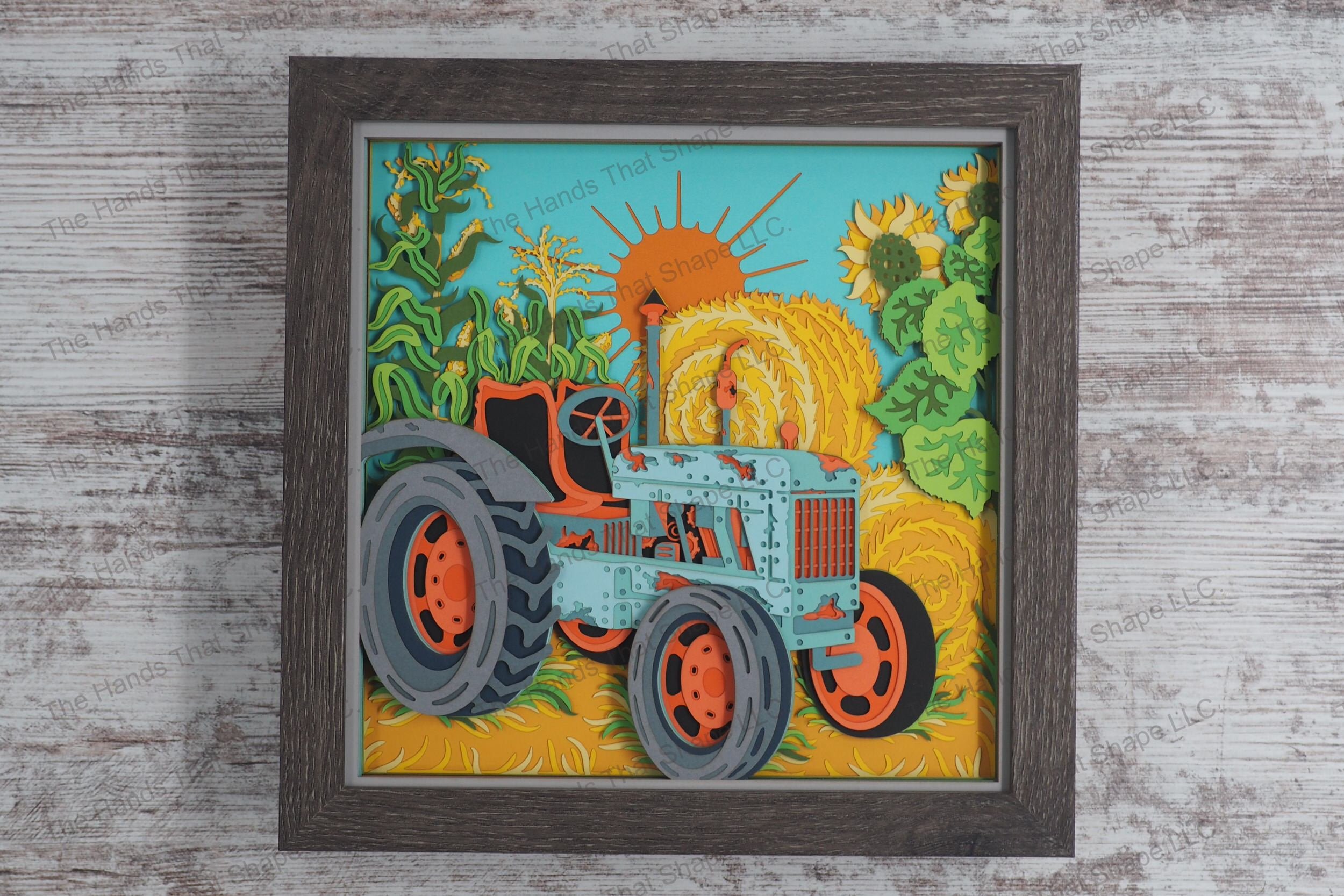 A detailed layered paper framed shadowbox depicting an old tractor surrounded by corn stalks, sunflowers, and hay bales under a setting sun.