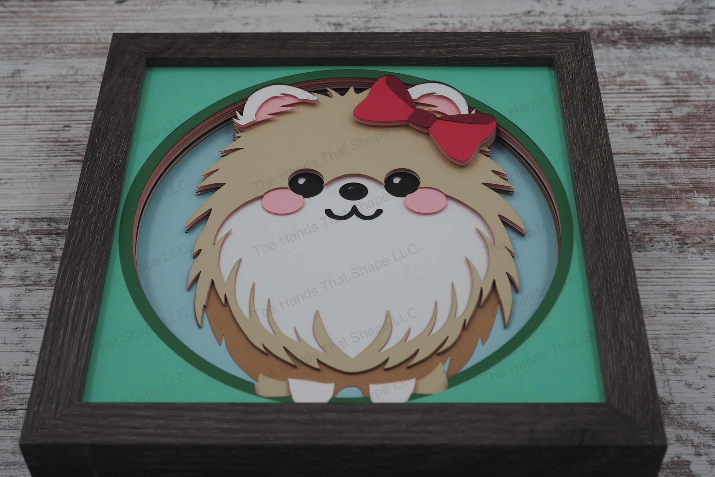 This delightful layered paper art shadowbox showcases an irresistibly fluffy Pomeranian dog with an oversized bow, crafted into a vibrant 3d display.