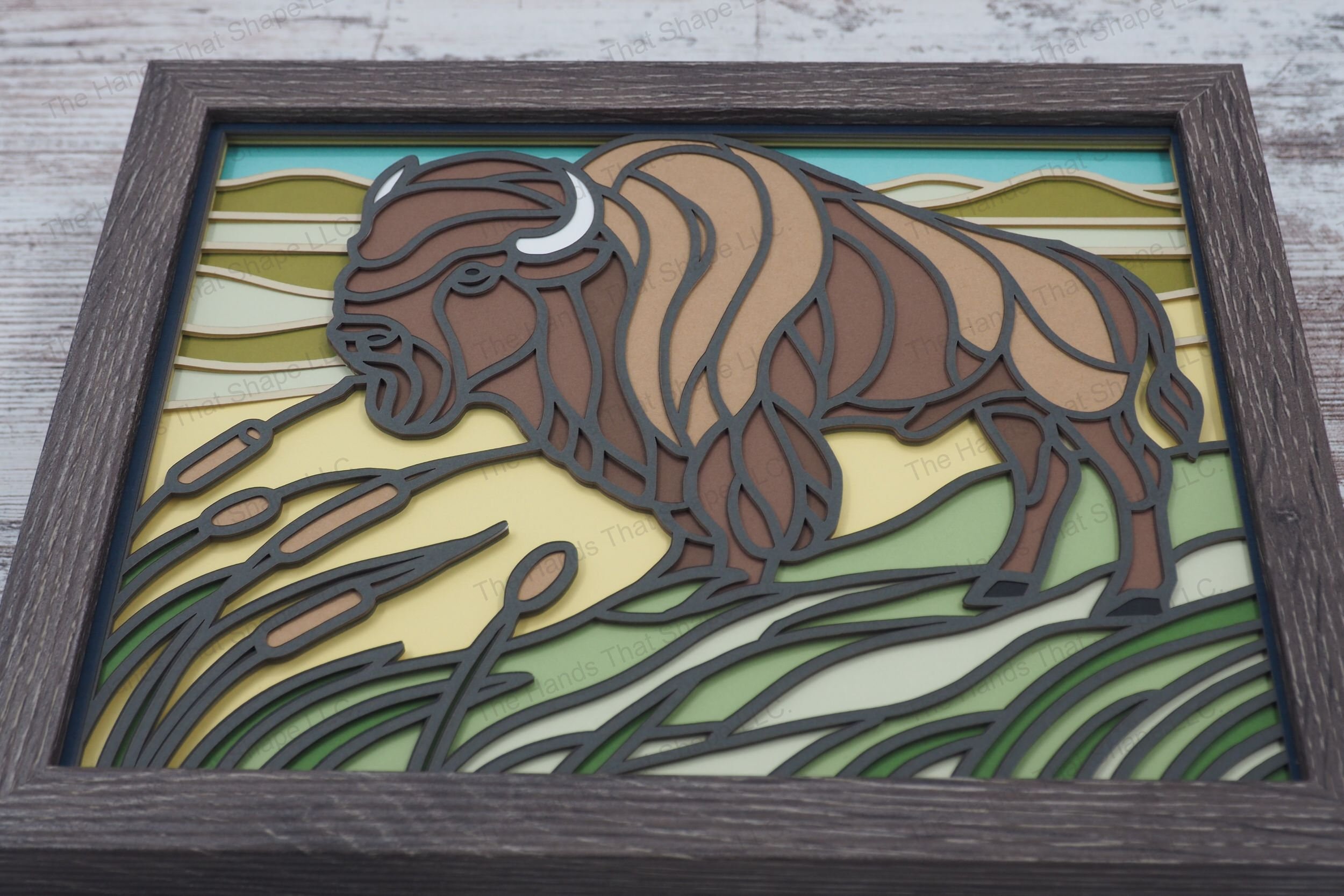 Discover the majestic presence of a bison depicted in stained glass style, standing on a prairie with rolling hills, encased in a glass-covered gray MDF frame.