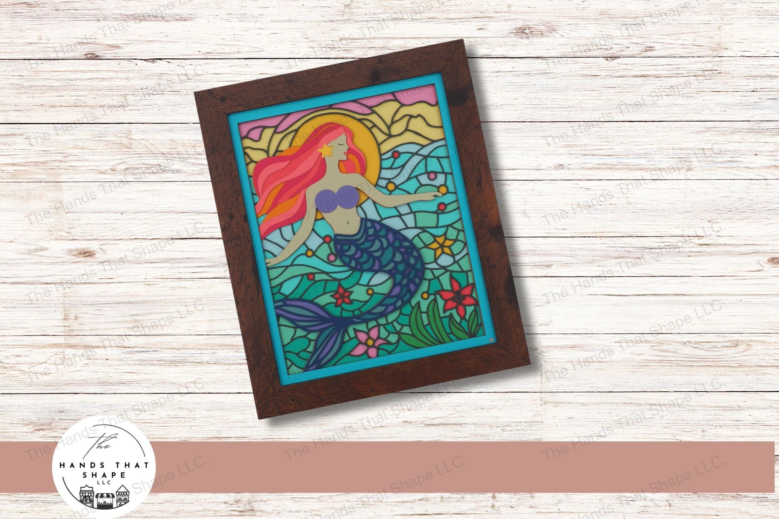 This layered cardstock art piece vividly captures a mystical mermaid with flowing hair, set against a backdrop of stained glass-style ocean blues and a sunrise.