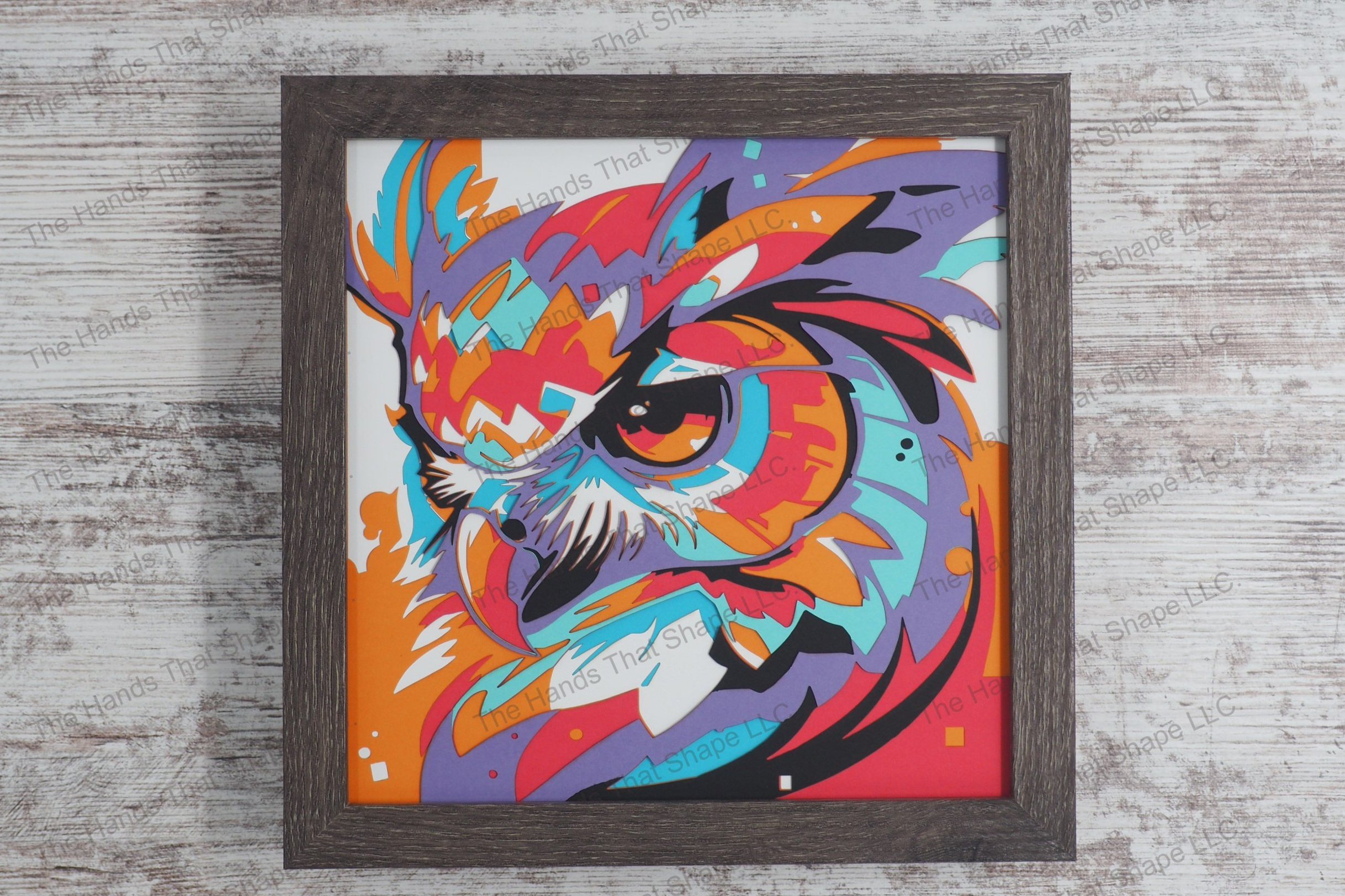 A vibrant layered paper shadowbox depicting the head of an owl in vivid colors, crafted from 7 layers of cardstock, encased in a gray MDF frame.