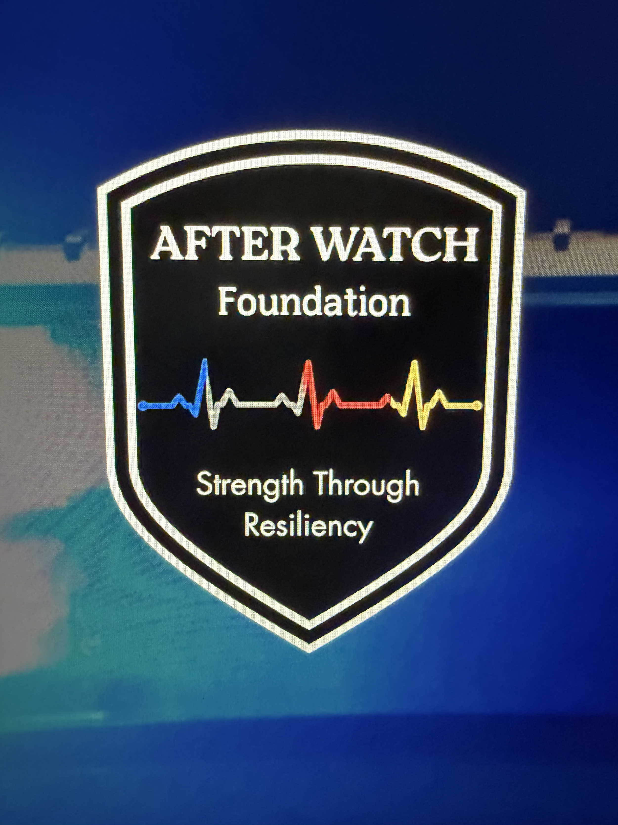 A shield-shaped logo with text that reads 'After Watch Foundation' and 'Strength Through Resiliency,' featuring a colorful heartbeat line design and a blue background.
