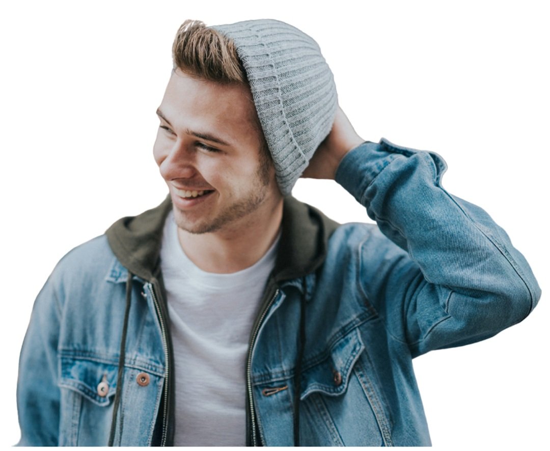 A young man smiling, wearing a gray beanie, denim jacket, and white t-shirt, touching the back of his head with his left hand.