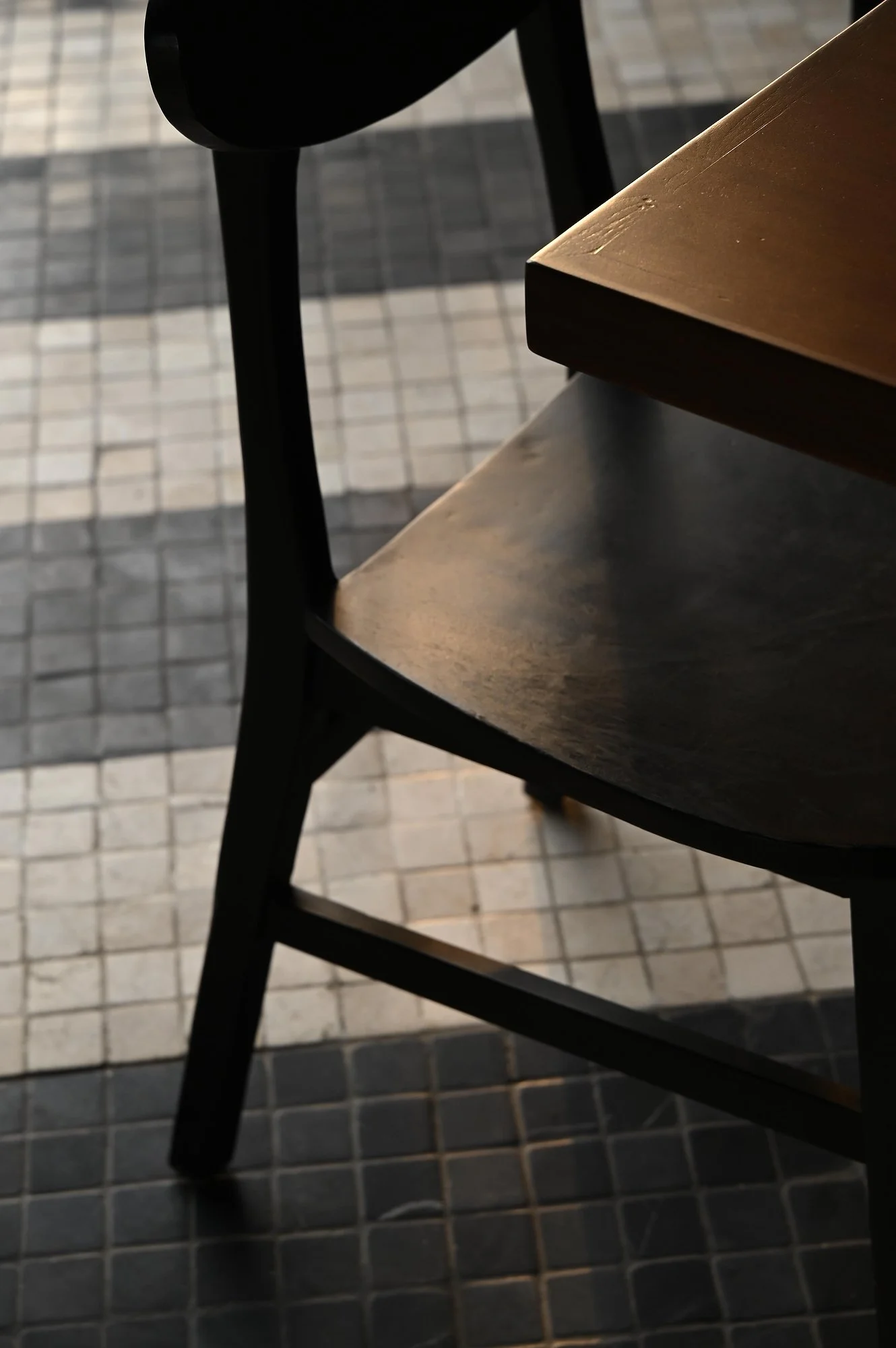 Close-up photo of wooden chairs with black metal frames on a tiled floor.