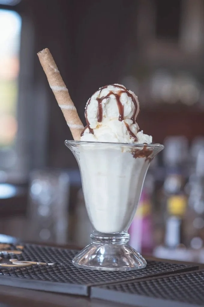 Vanilla ice cream sundae with chocolate drizzle, topped with a cherry on a glass dish, garnished with a wafer roll.