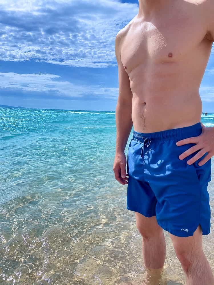 mann traegt nachhaltige badeshorts in blau am strand