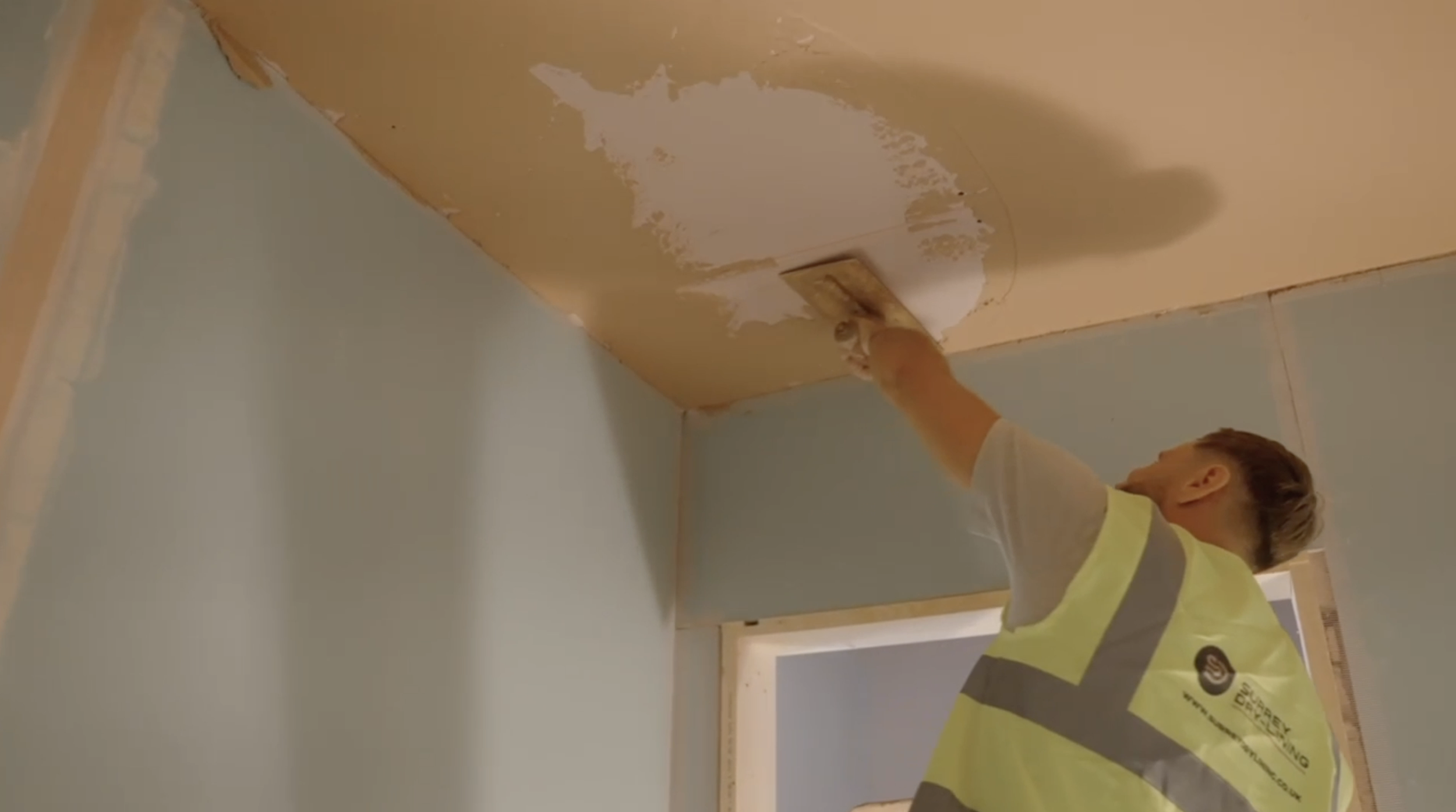 man wearing surrey drylining hi vis vest plastering a ceiling