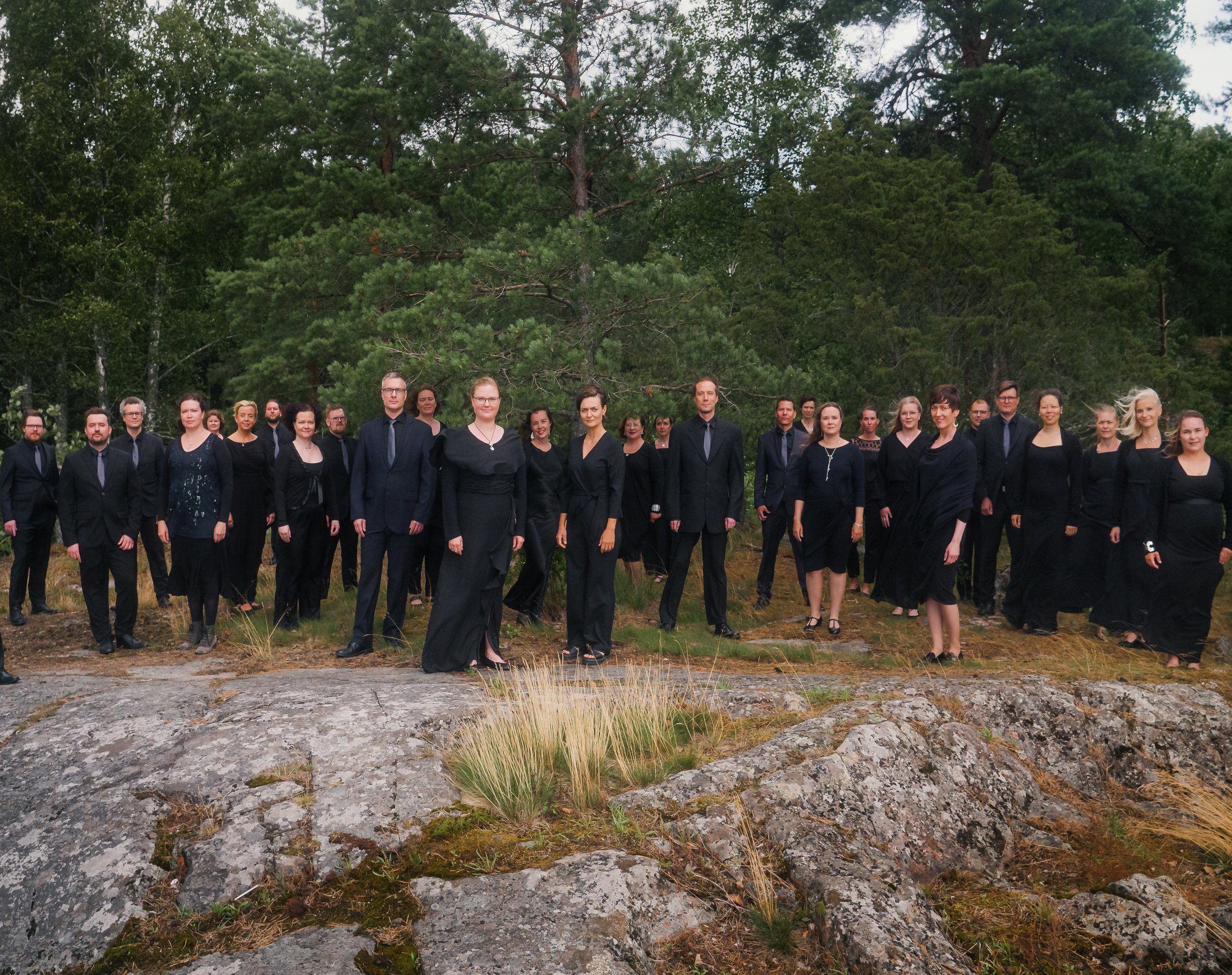 Kamarikuoro Audite seisoo tuulessa metsäisen kallion päällä