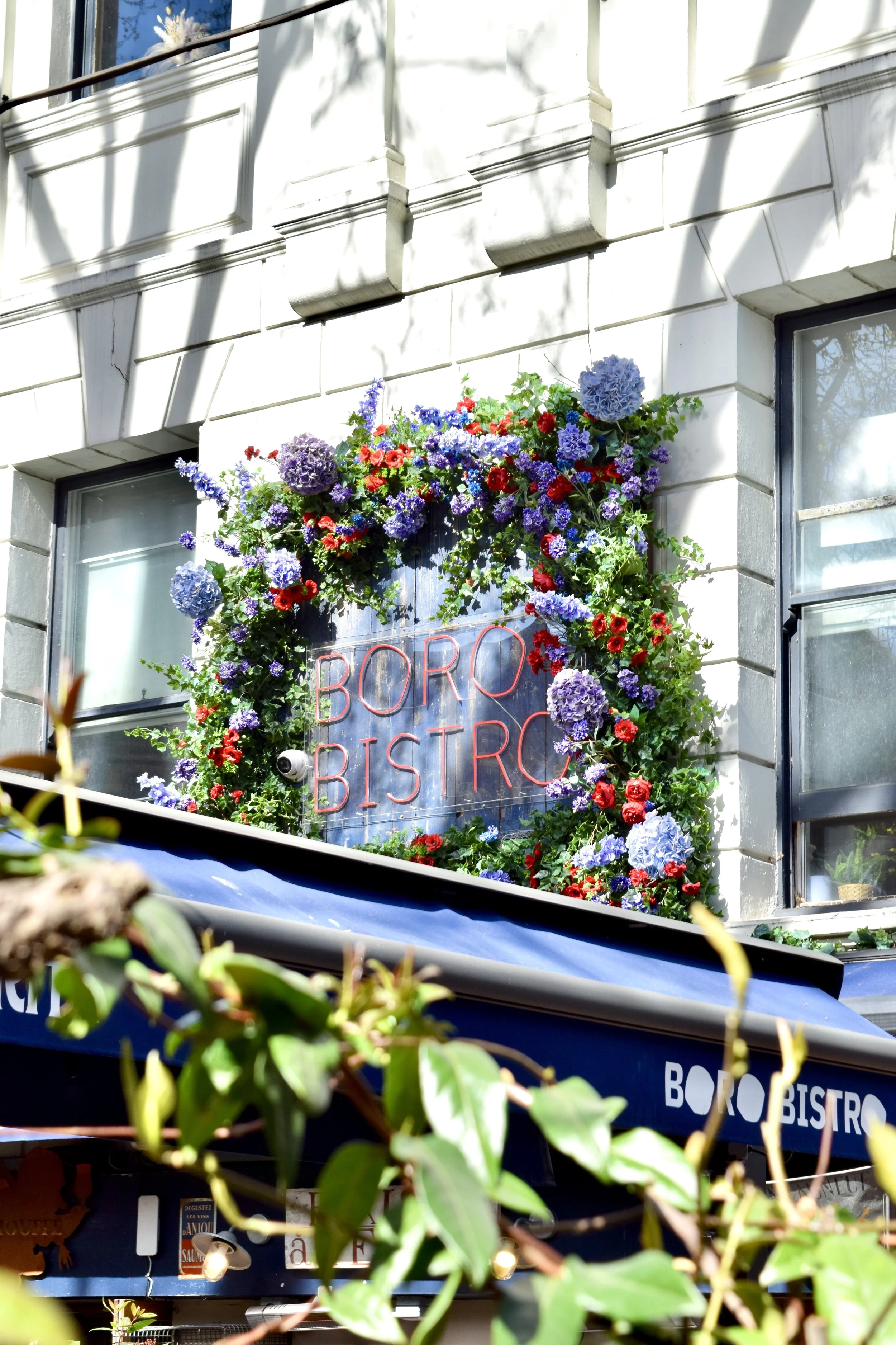 A sign for BORO BISTRO surrounded by a colorful flower wreath on the building's exterior with windows and an awning in the background.