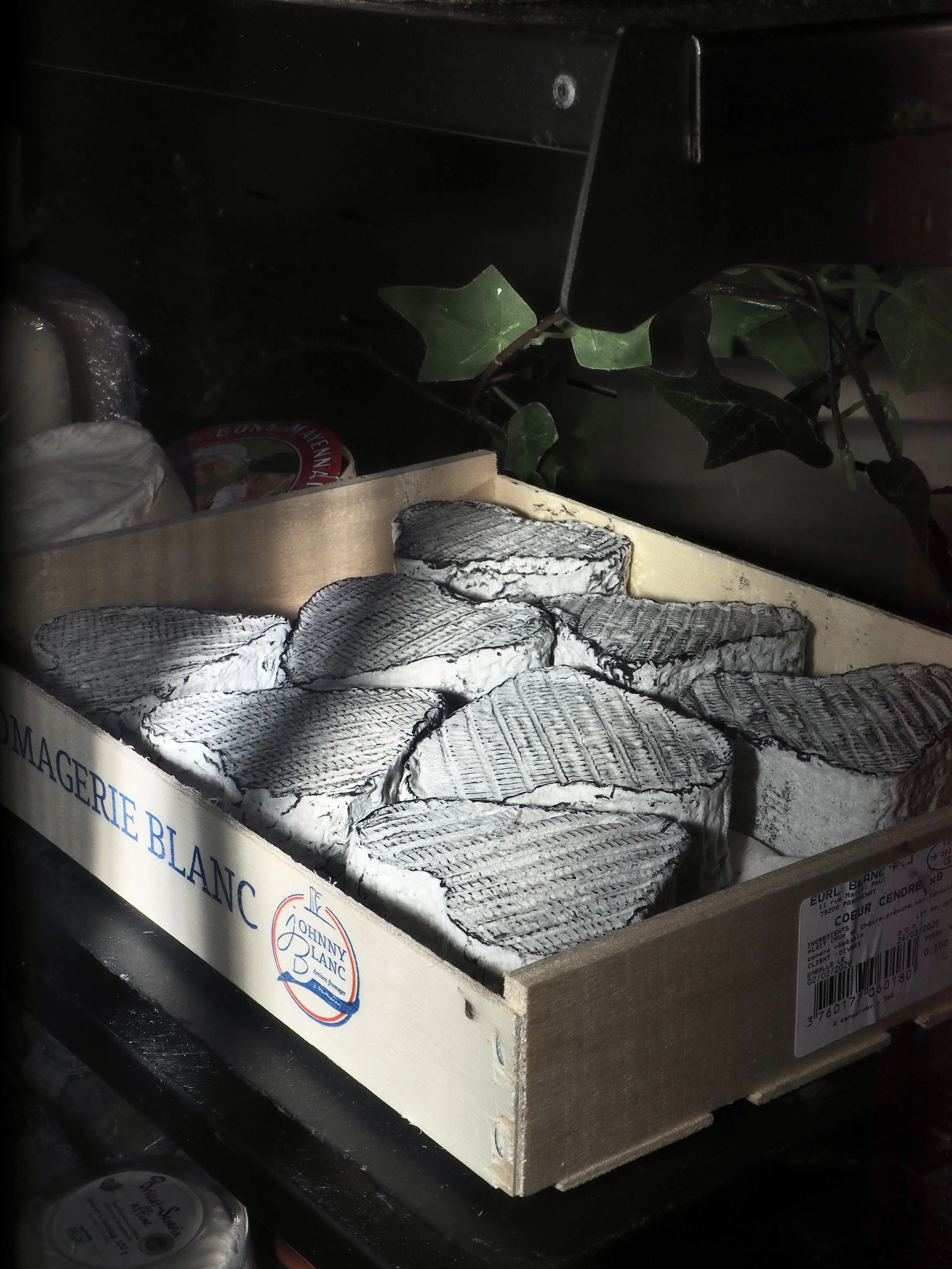 A wooden box with the label "FROMAGERIE BLANC" containing multiple pieces of Camembert cheese with white mold rind.
