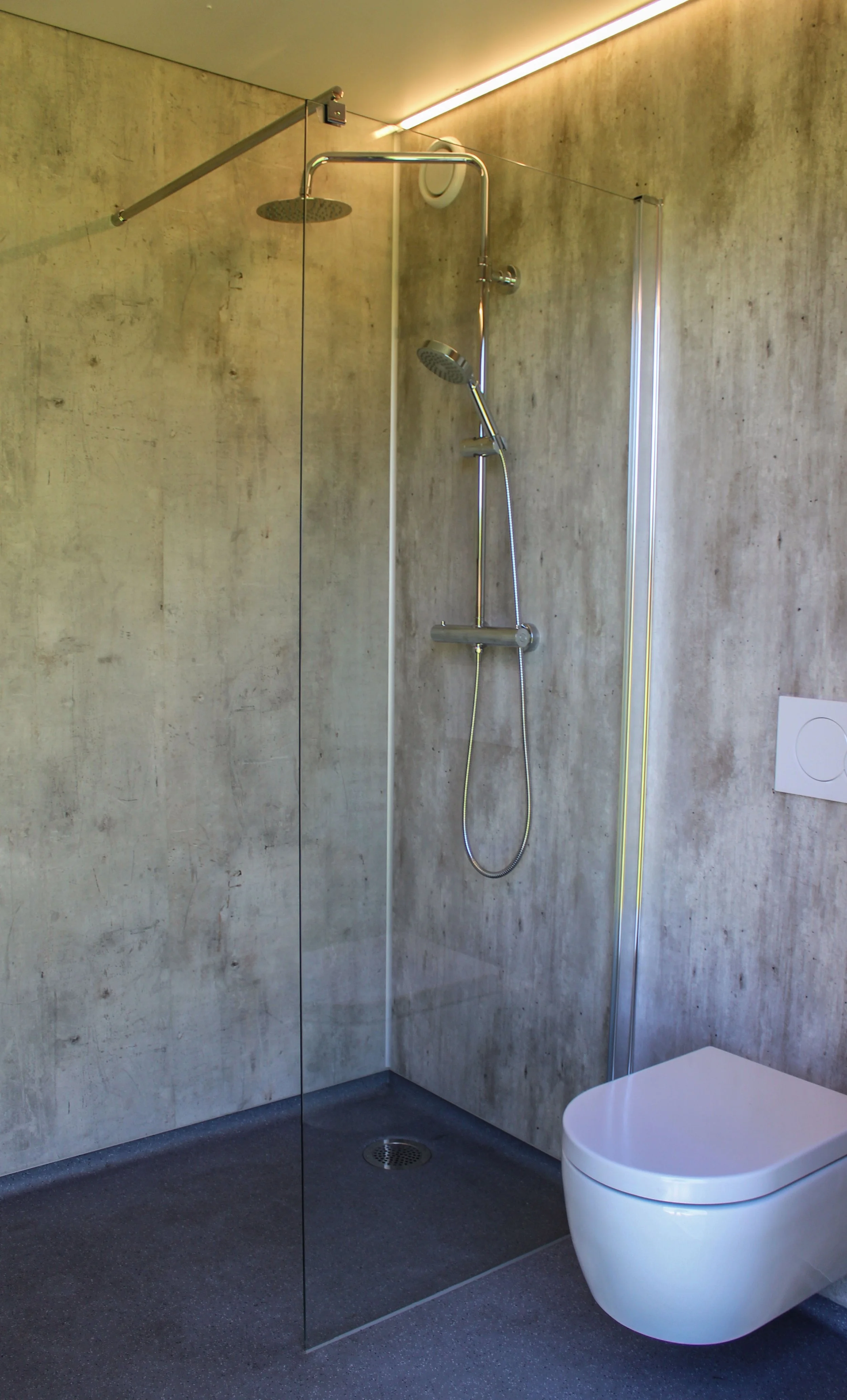 Ruime douchecabine met toilet. De betonlook wanden zijn onderhoudsarm