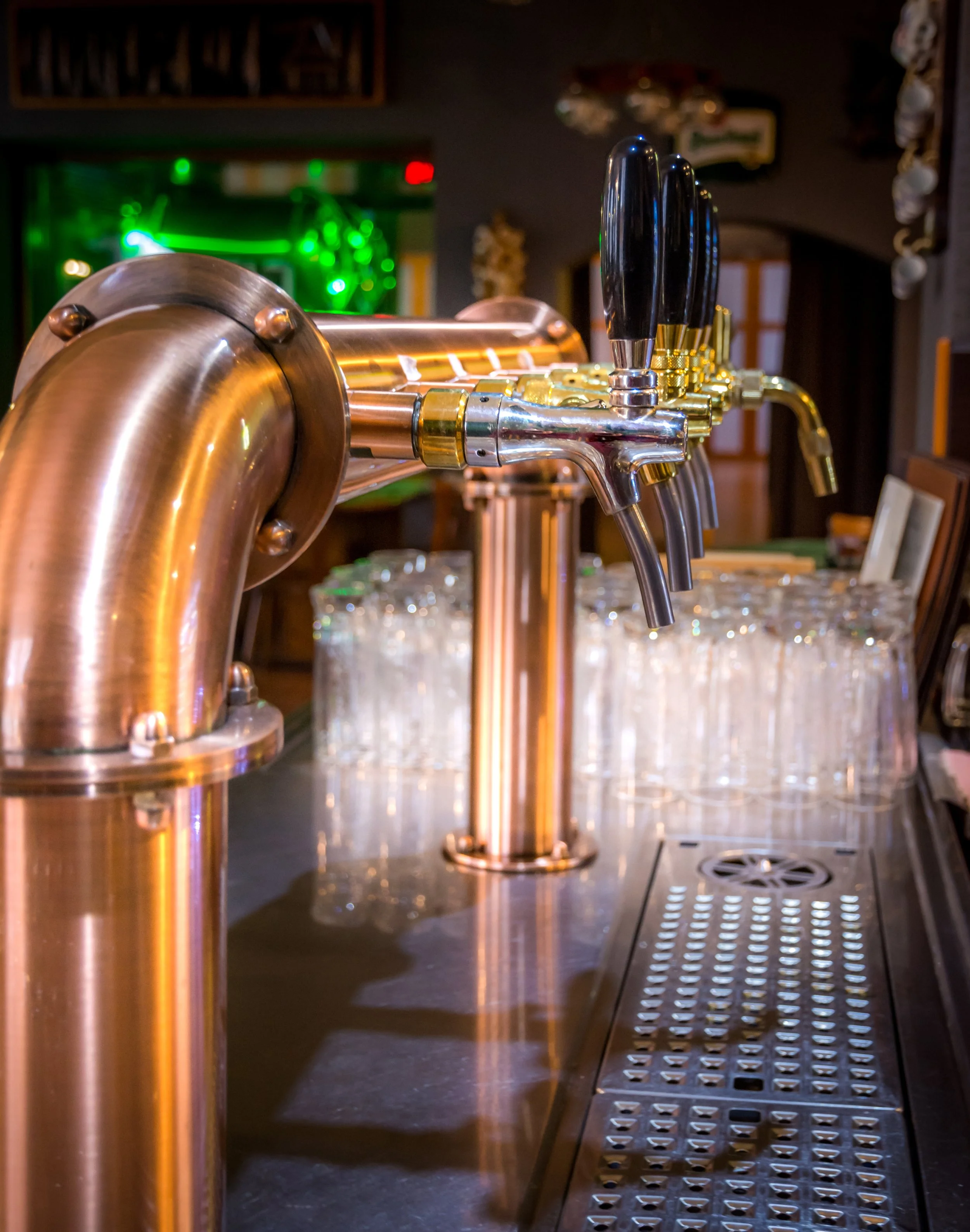 Copper beer tap handles and spouts at a bar with glassware in the background.