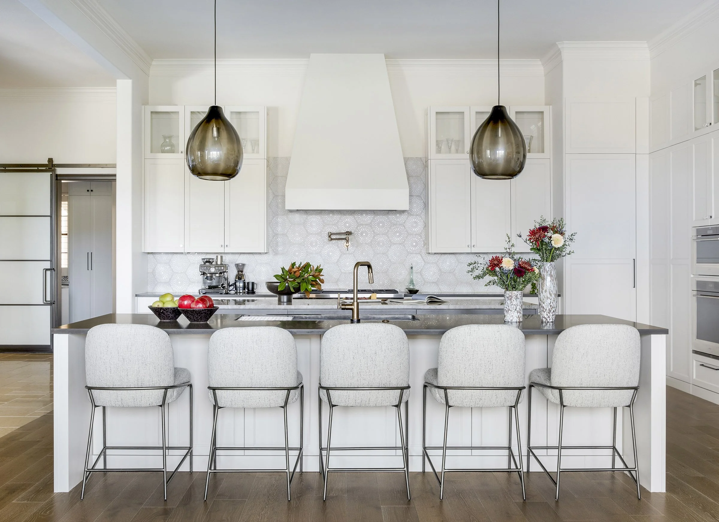 Kitchen with large island, hexagonal tile backsplash, pendant lighting, and white cabinetry with glass uppers