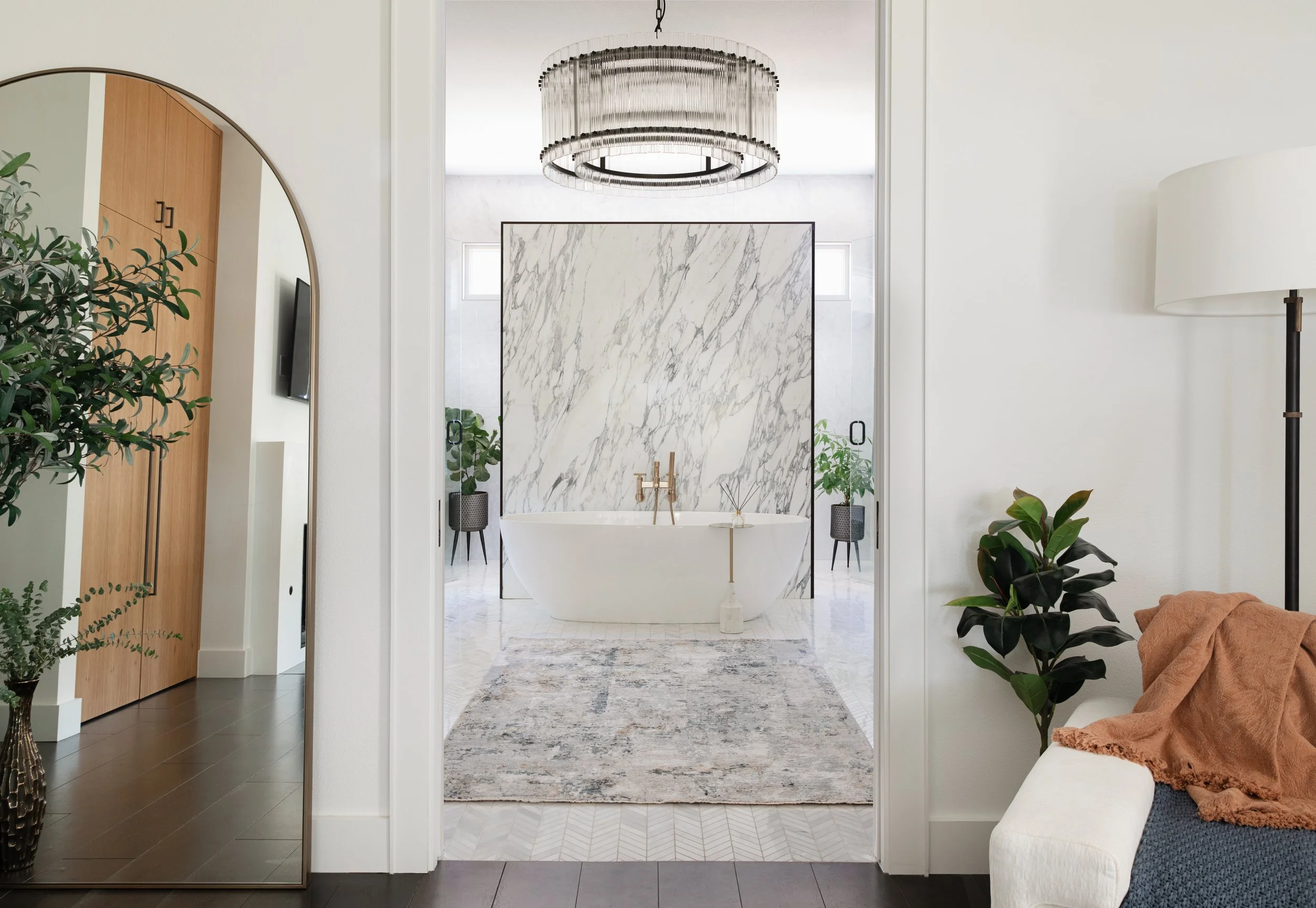 Primary bathroom with freestanding tub, marble wall, and modern chandelier lighting