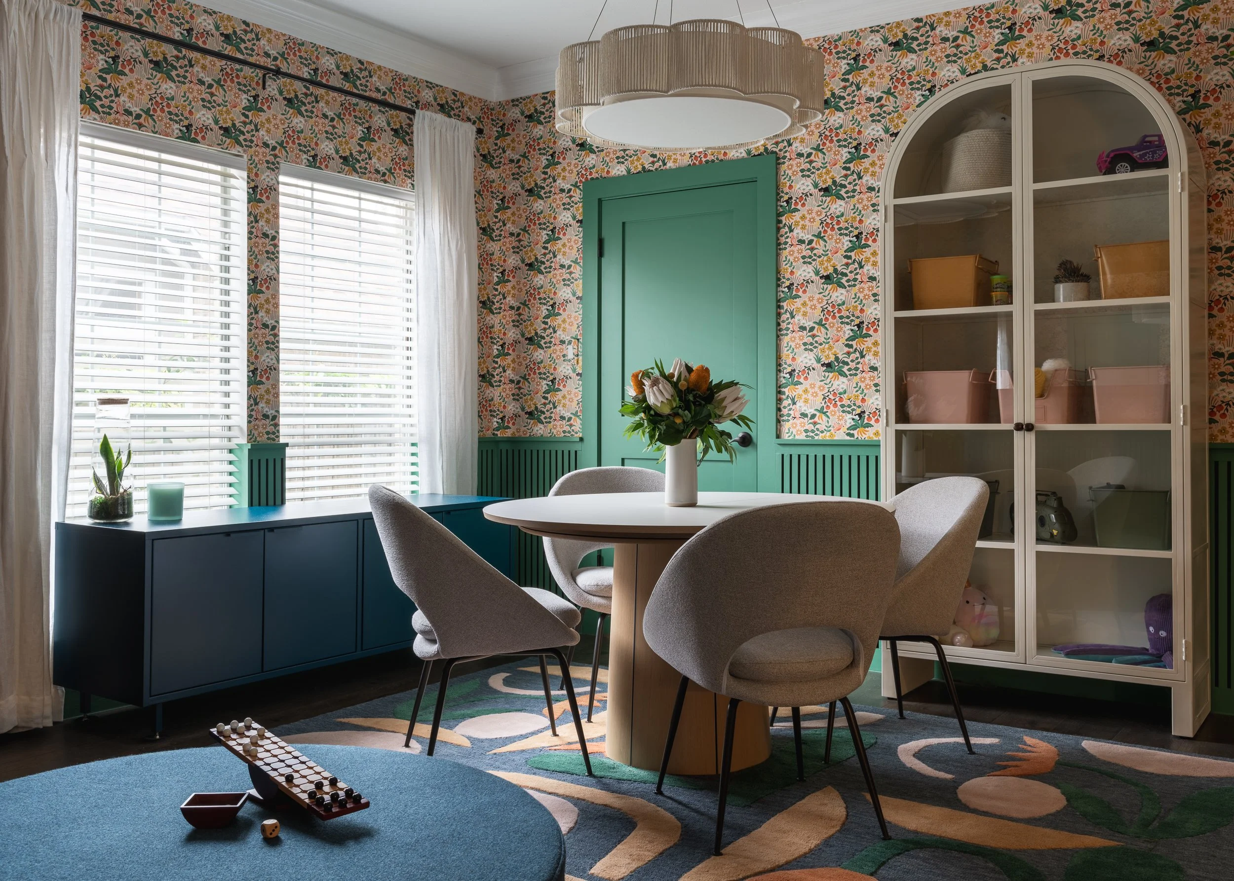 Retro modern dining room with floral wallpaper, green trim, a round table with four chairs, and contemporary storage solutions with a bold geometric floor rug