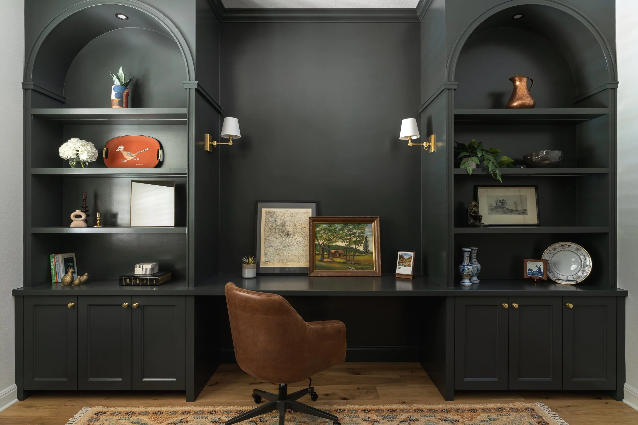Built-in home office with charcoal-colored cabinetry, arched shelves, desktop, and wood floors