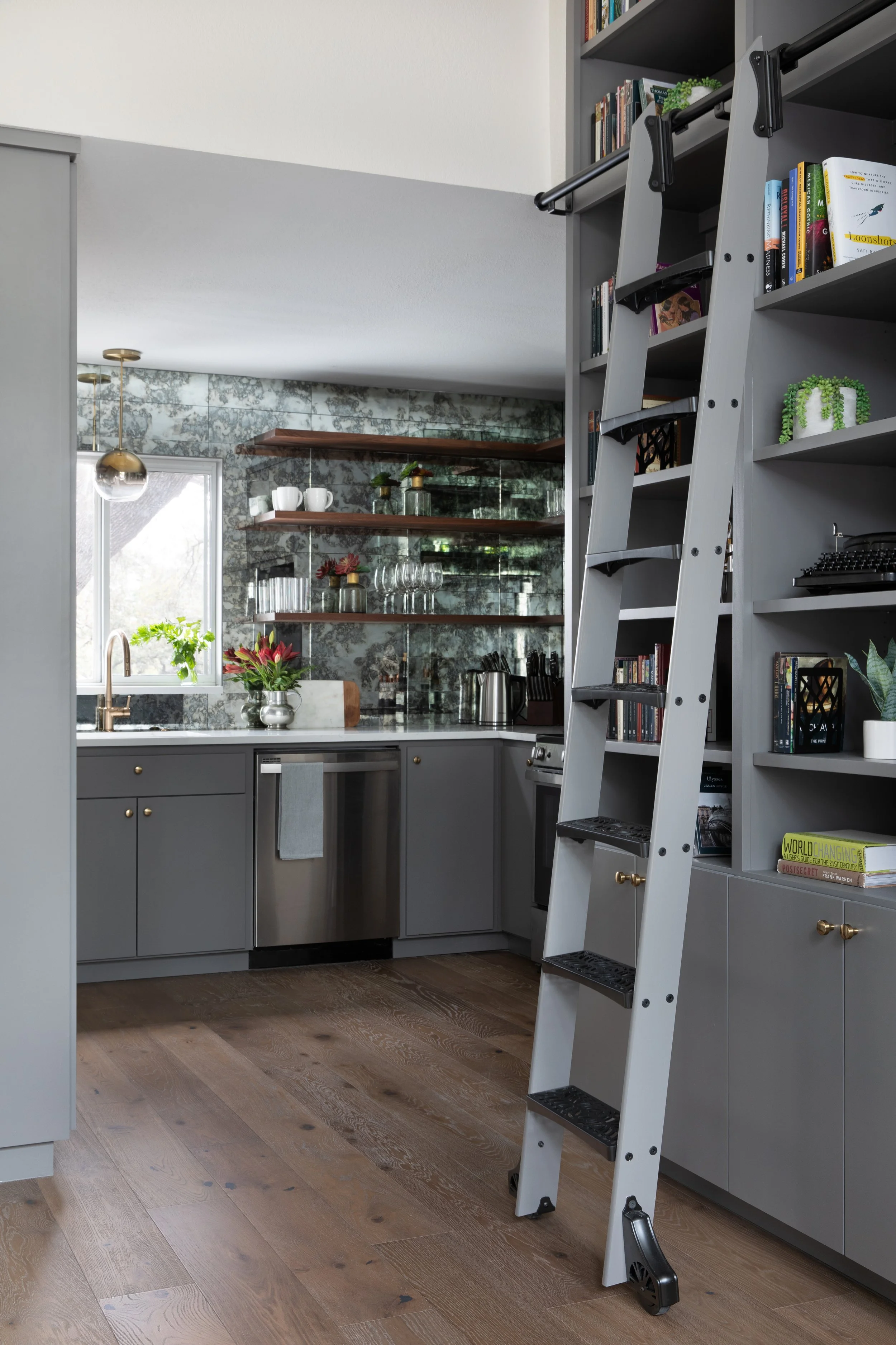 Kitchen with gray cabinetry, open shelving, and rolling library ladder accessing storage