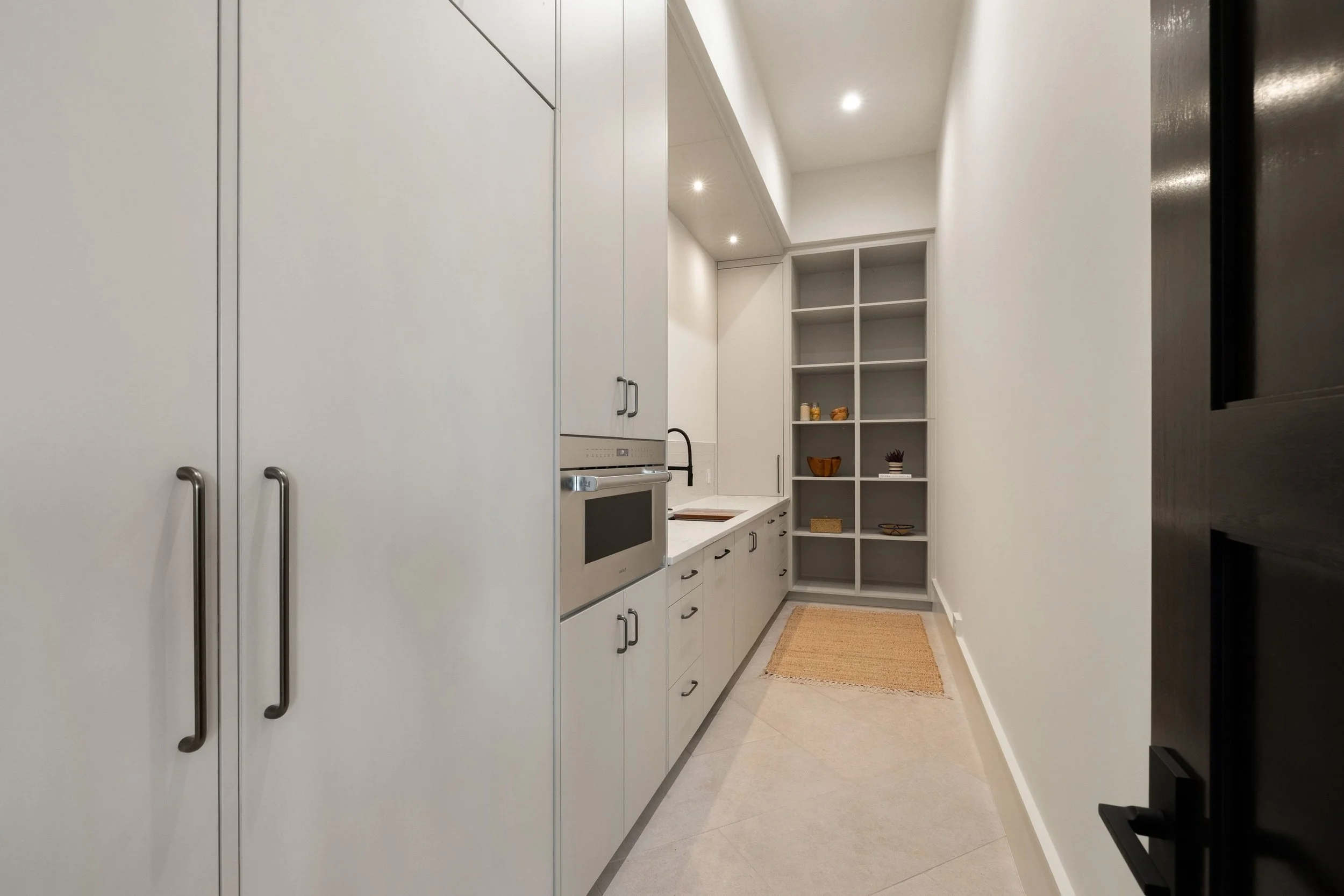 Pantry cabinetry with integrated appliances, open shelving, and natural wood accents