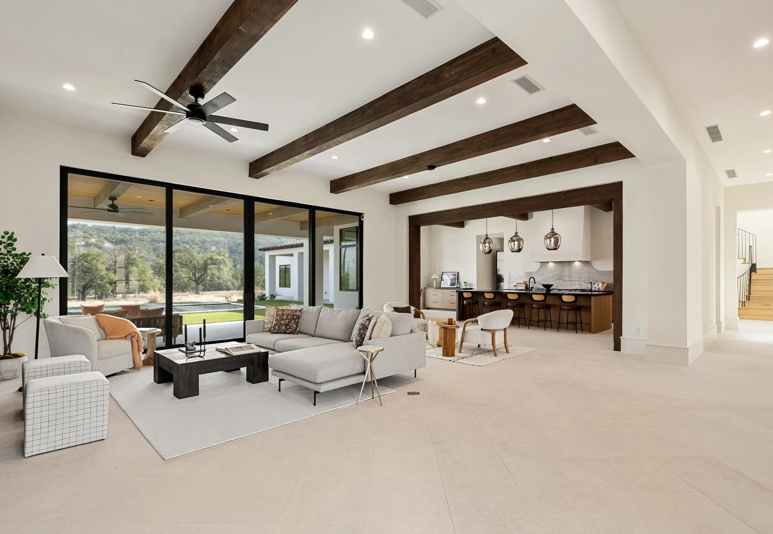 Open-concept living room looking with wooden ceiling beams looking into kitchen and dining area
