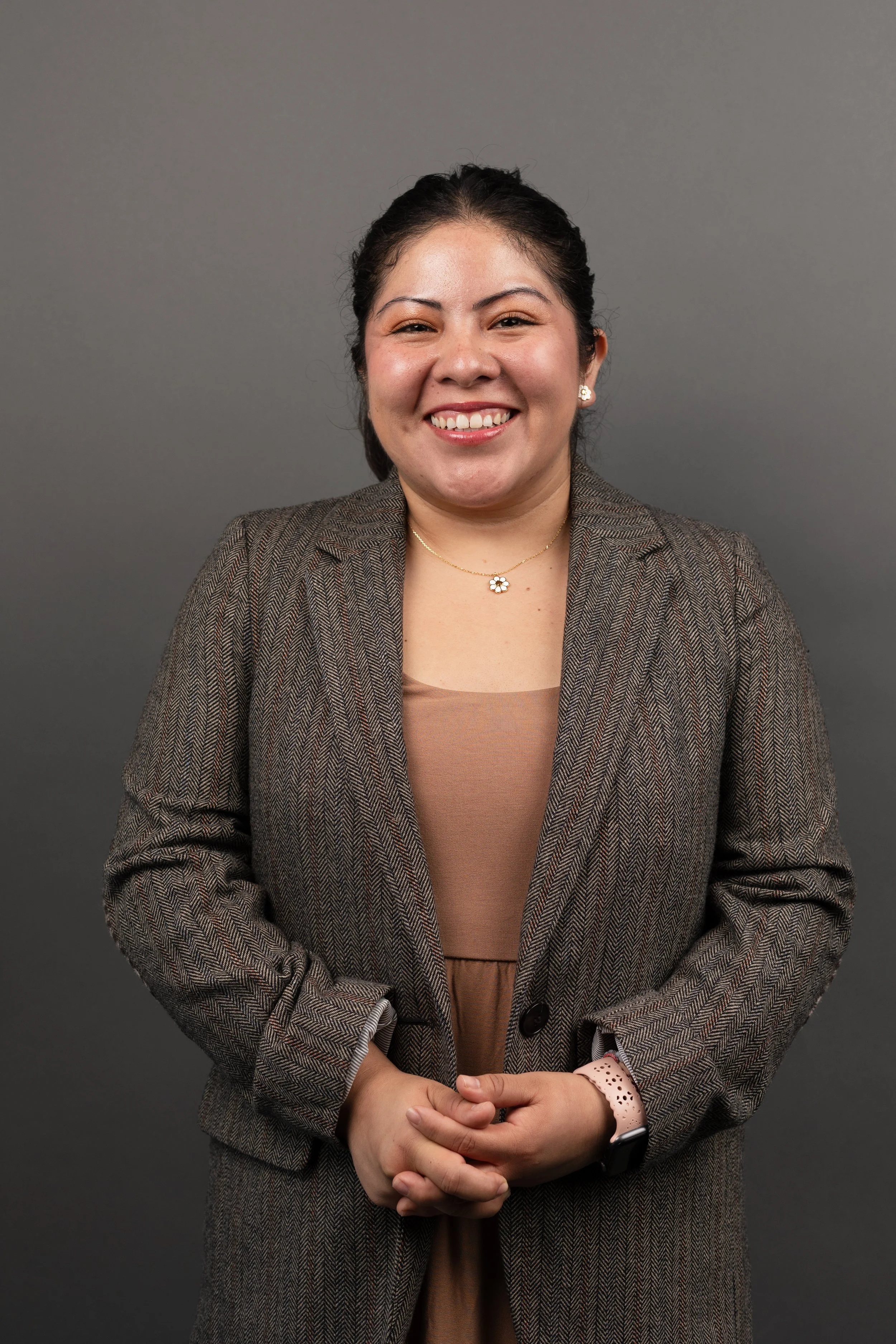 A woman smiling in a professional outfit against a gray background.