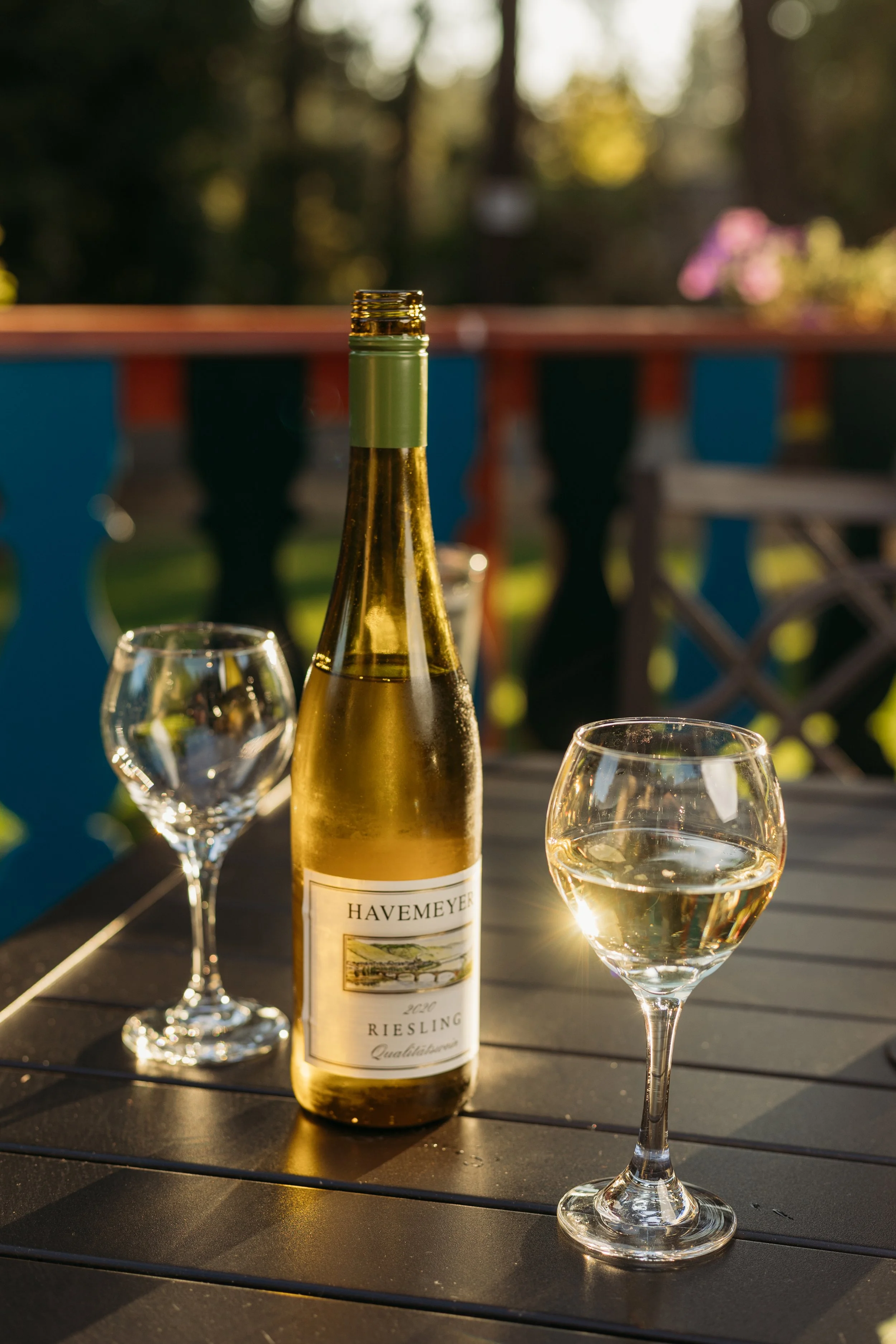 A bottle of Havemeyer Riesling wine with two glasses of white wine on a dark outdoor table during sunset.