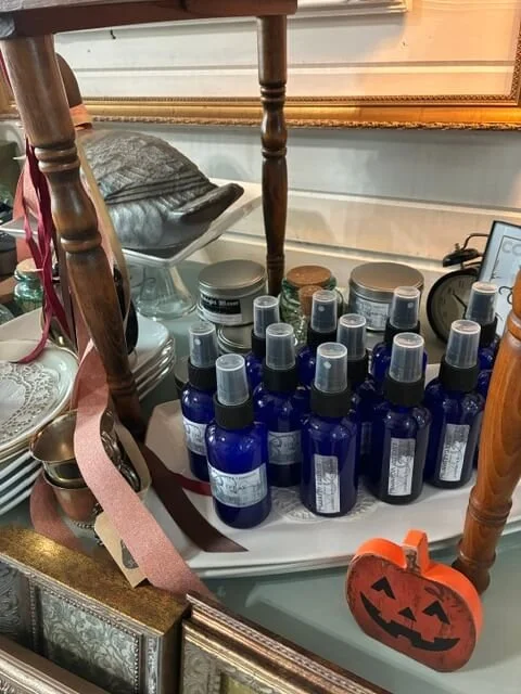 A collection of small blue spray bottles with gray caps on a mirror top table, with Halloween-themed decorations nearby.