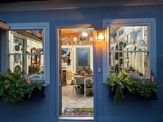 View through a front door into a cozy, decorated interior with plants and American flags outside the windows.