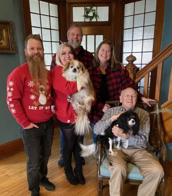 Family of four people with two dogs posing indoors during Christmas time.