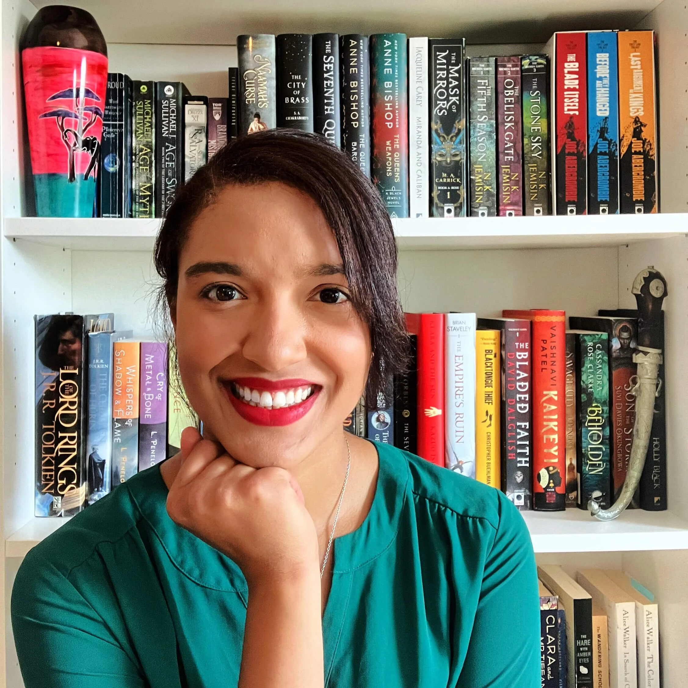 Book coach & fiction editor, Olivia Bedford, sits in front of a bookshelf of fantasy novels looking forward and smiling.