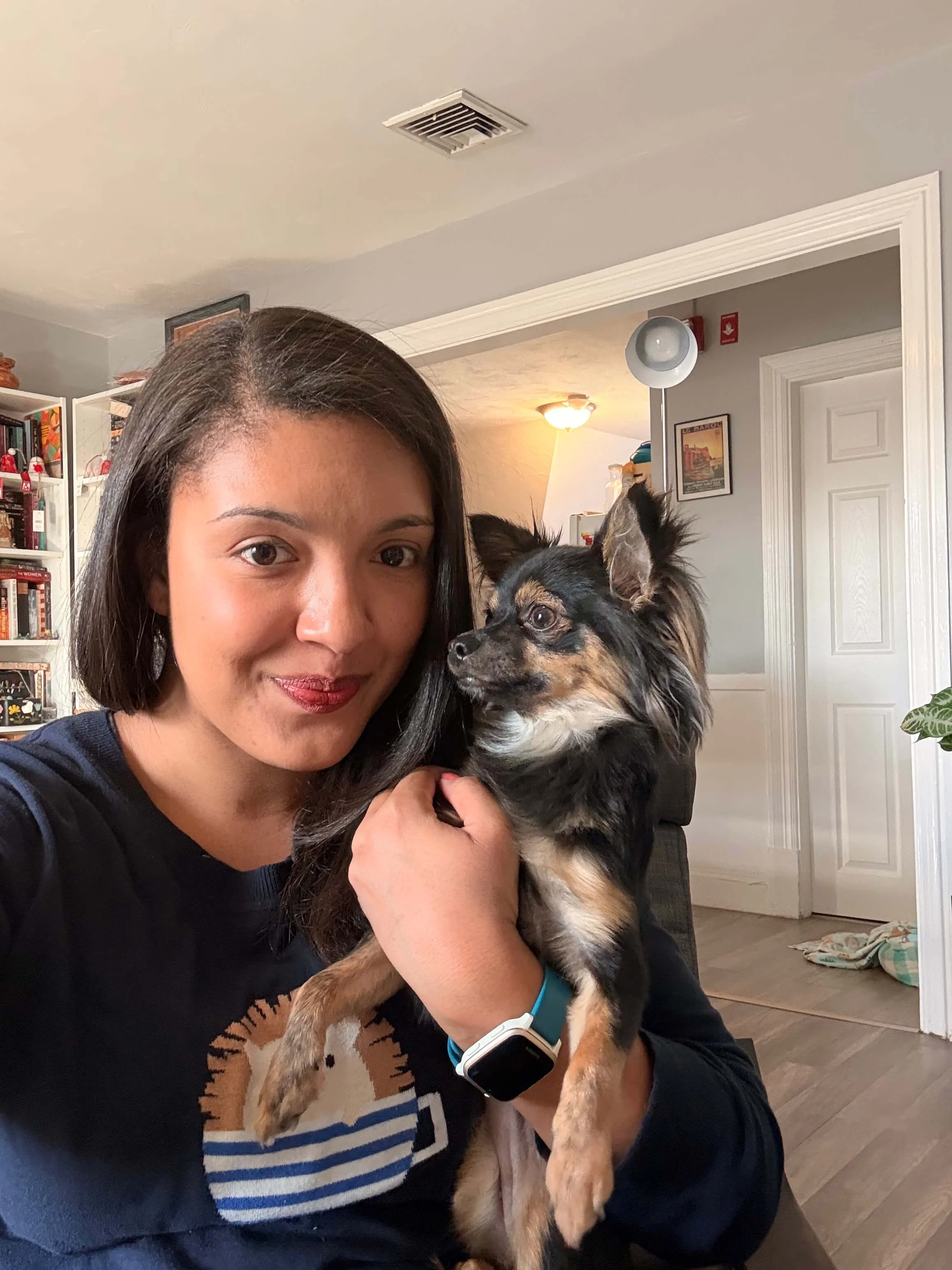 Book coach & editor, Olivia Bedford, sits smiling at the camera wearing a hedgehog sweater and holding her chihuahua, Minerva.