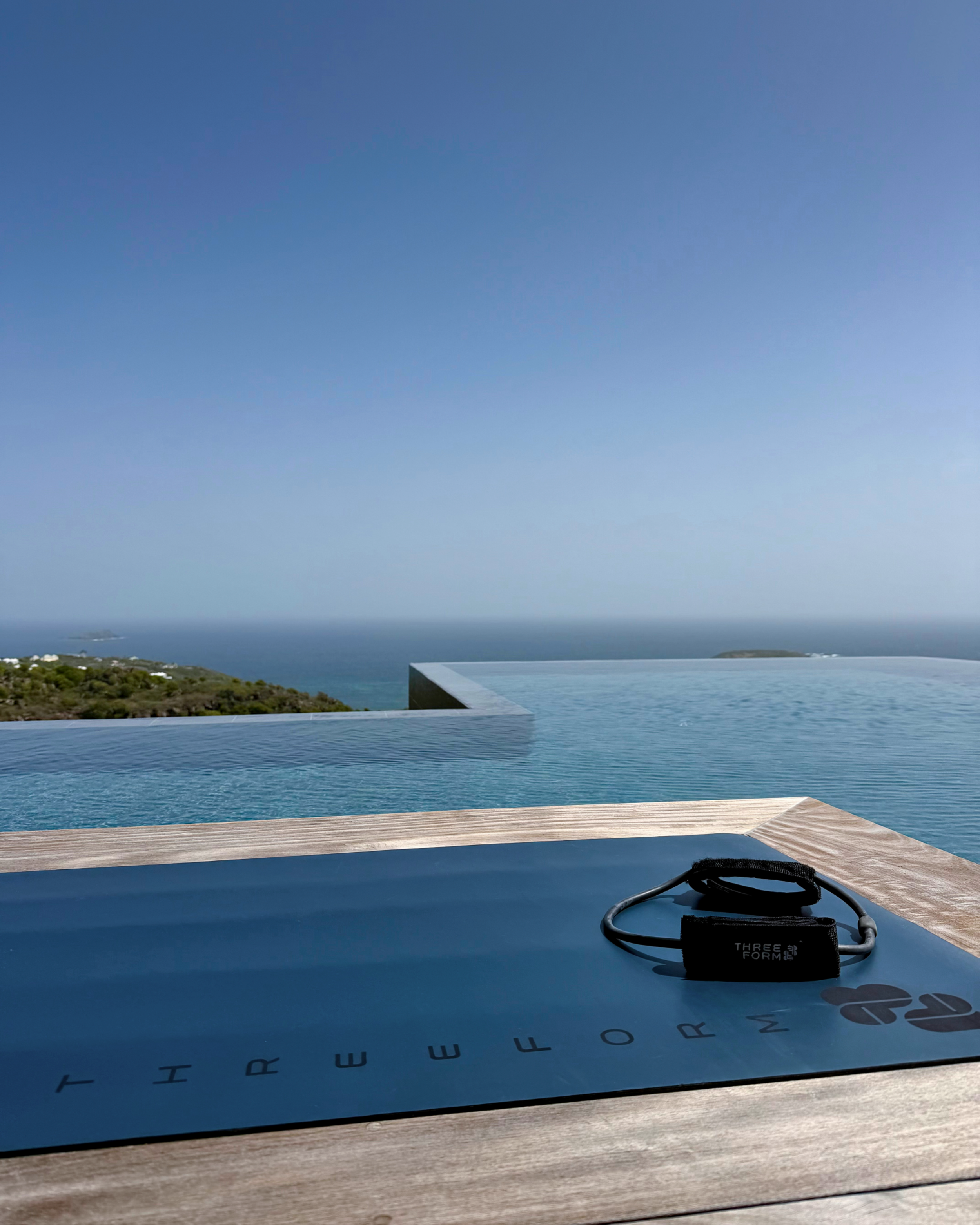 View of a swimming pool with a city and ocean in the background, a wristwatch, and an electrical device on the wooden deck.